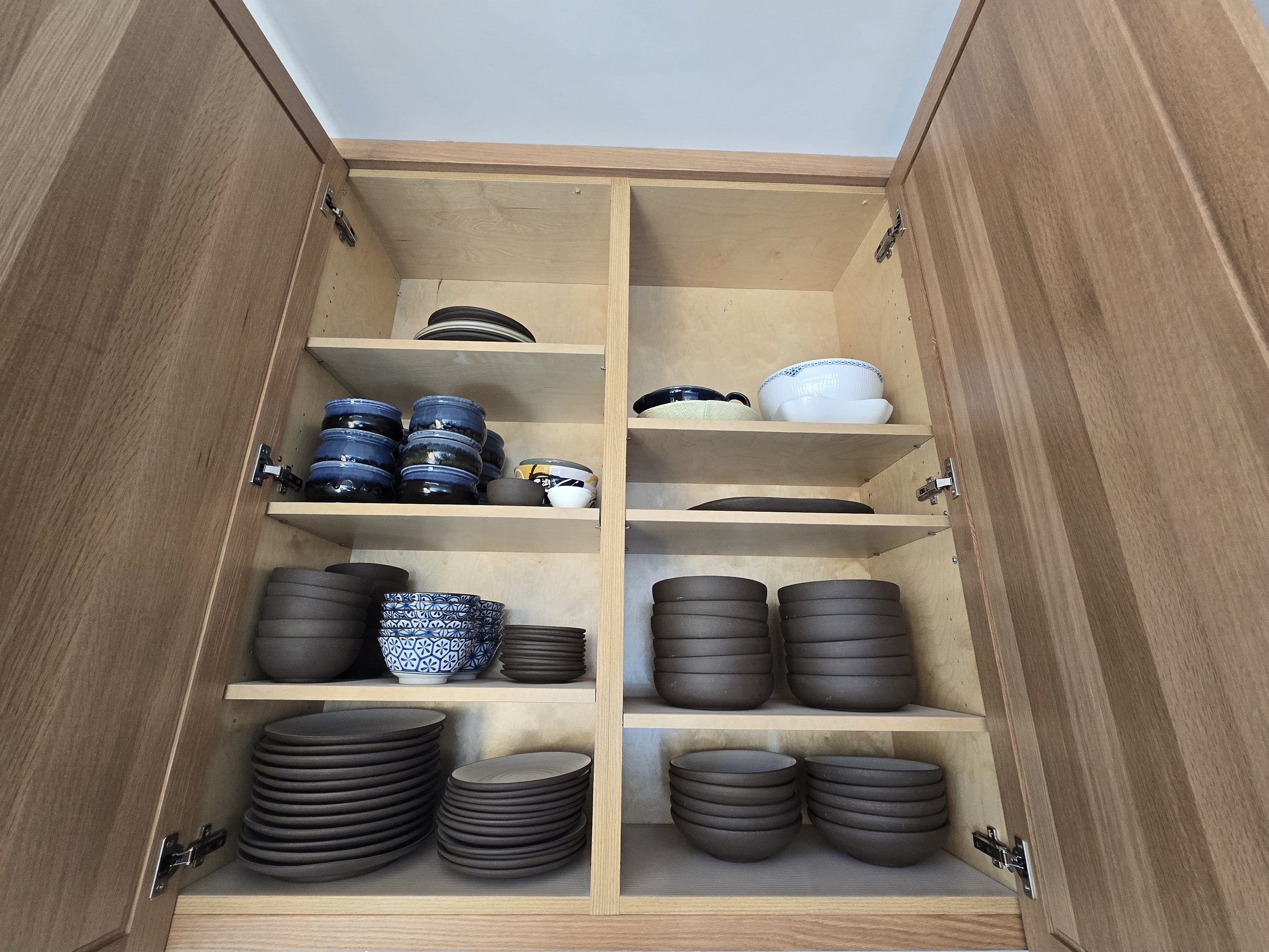 Open kitchen cabinet filled with ceramic bowls and dishes of various sizes and colors, neatly stacked on shelves.