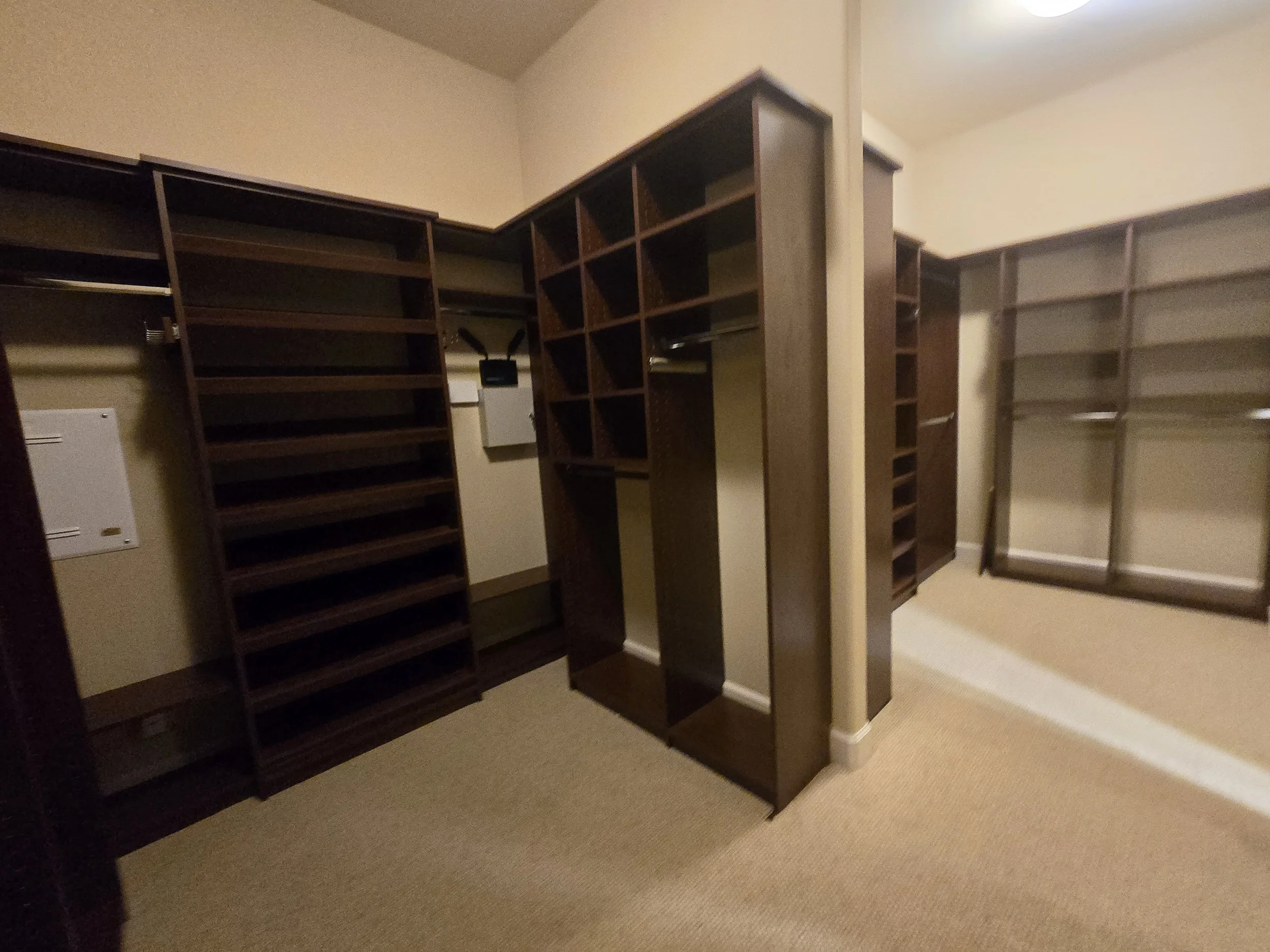 Empty walk-in closet with dark wooden shelves, racks for hanging clothes, and a sliding glass door.