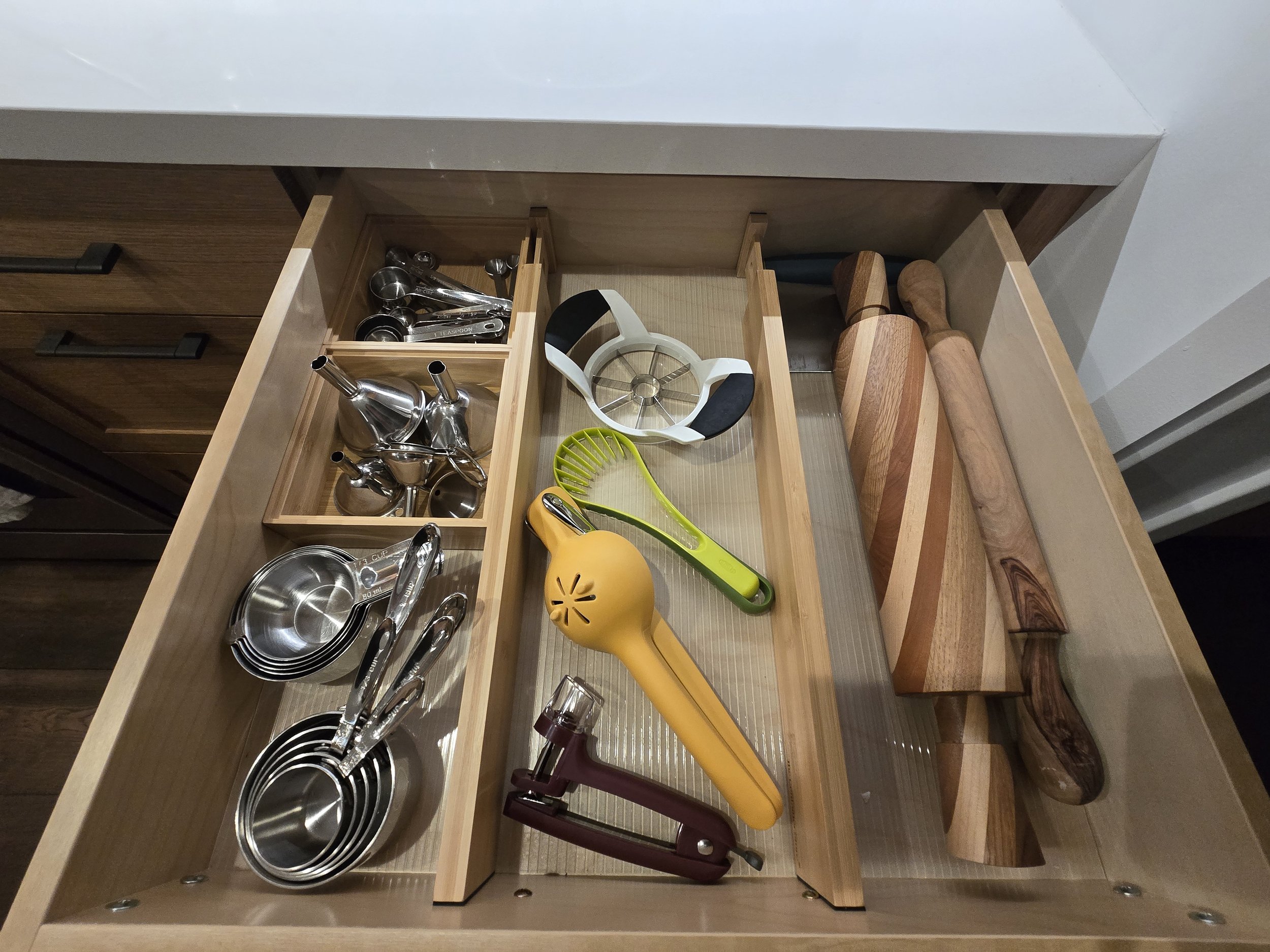 Kitchen drawer containing measuring spoons, a pizza cutter, a lemon squeezer, a garlic press, wooden cutting boards, and some knives.