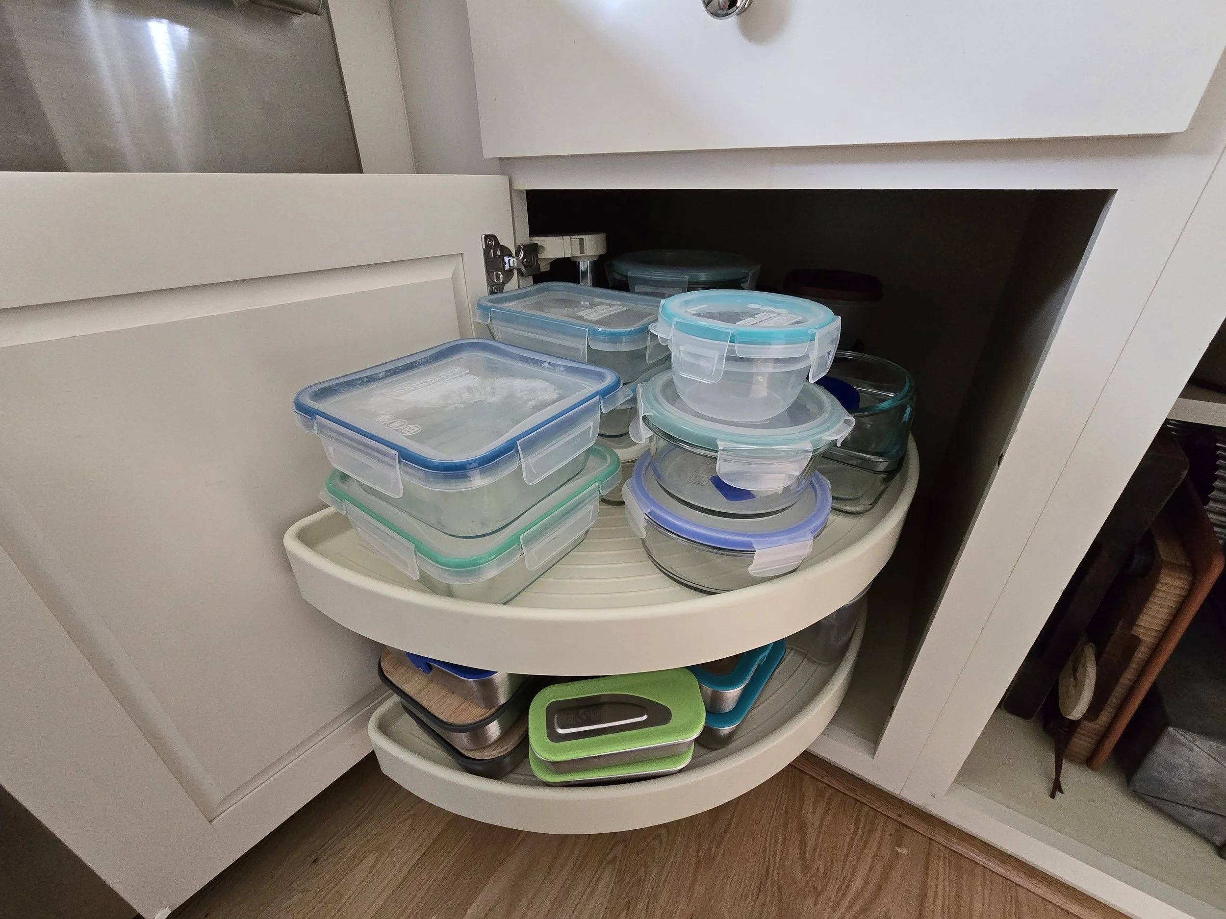 Open kitchen cabinet with various glass and plastic food storage containers stacked inside.