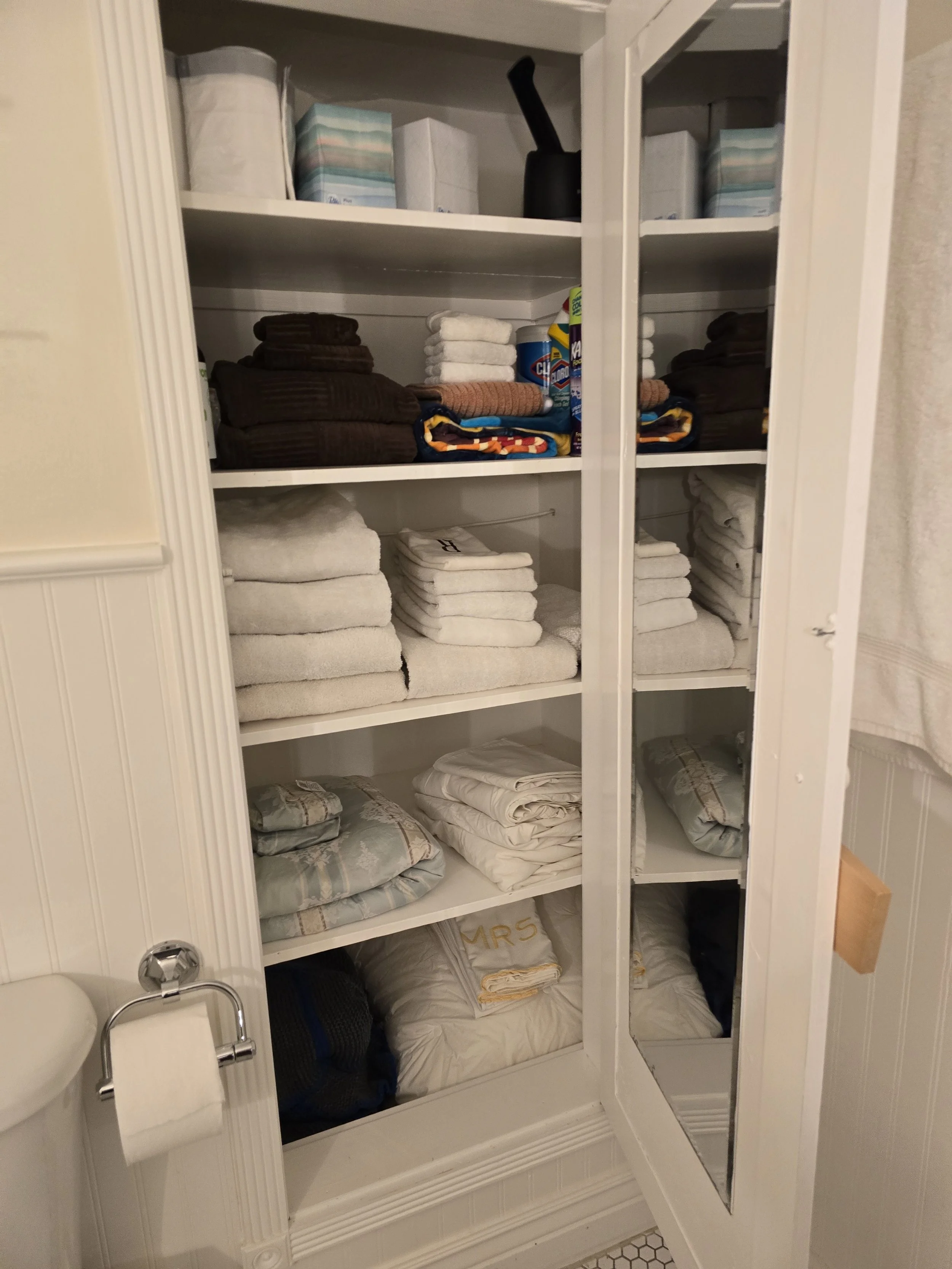 Shelves filled with folded towels, blankets, and laundry supplies in a bathroom cabinet.
