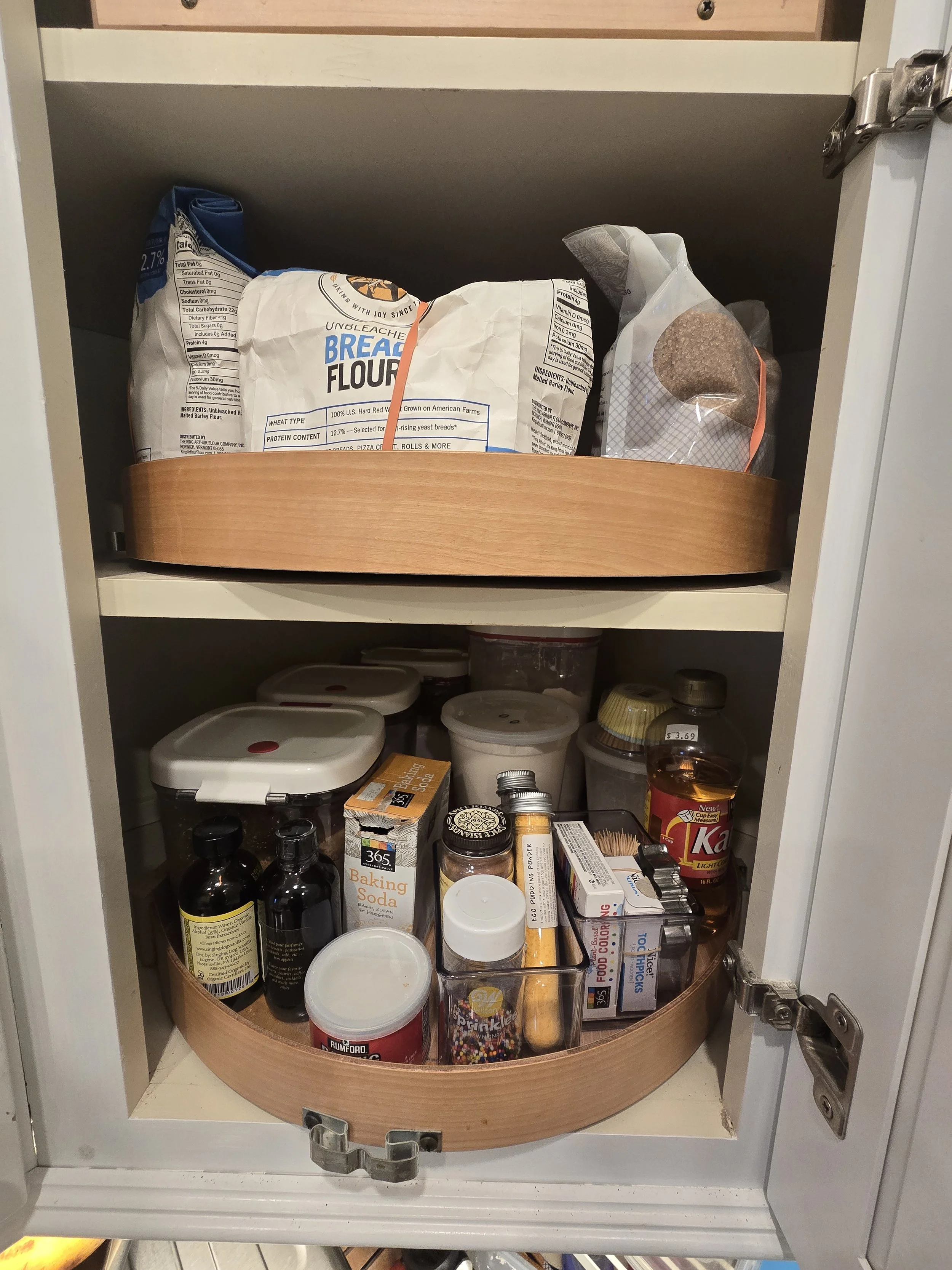Open kitchen cabinet with two shelves containing baking supplies, food, and drinks.
