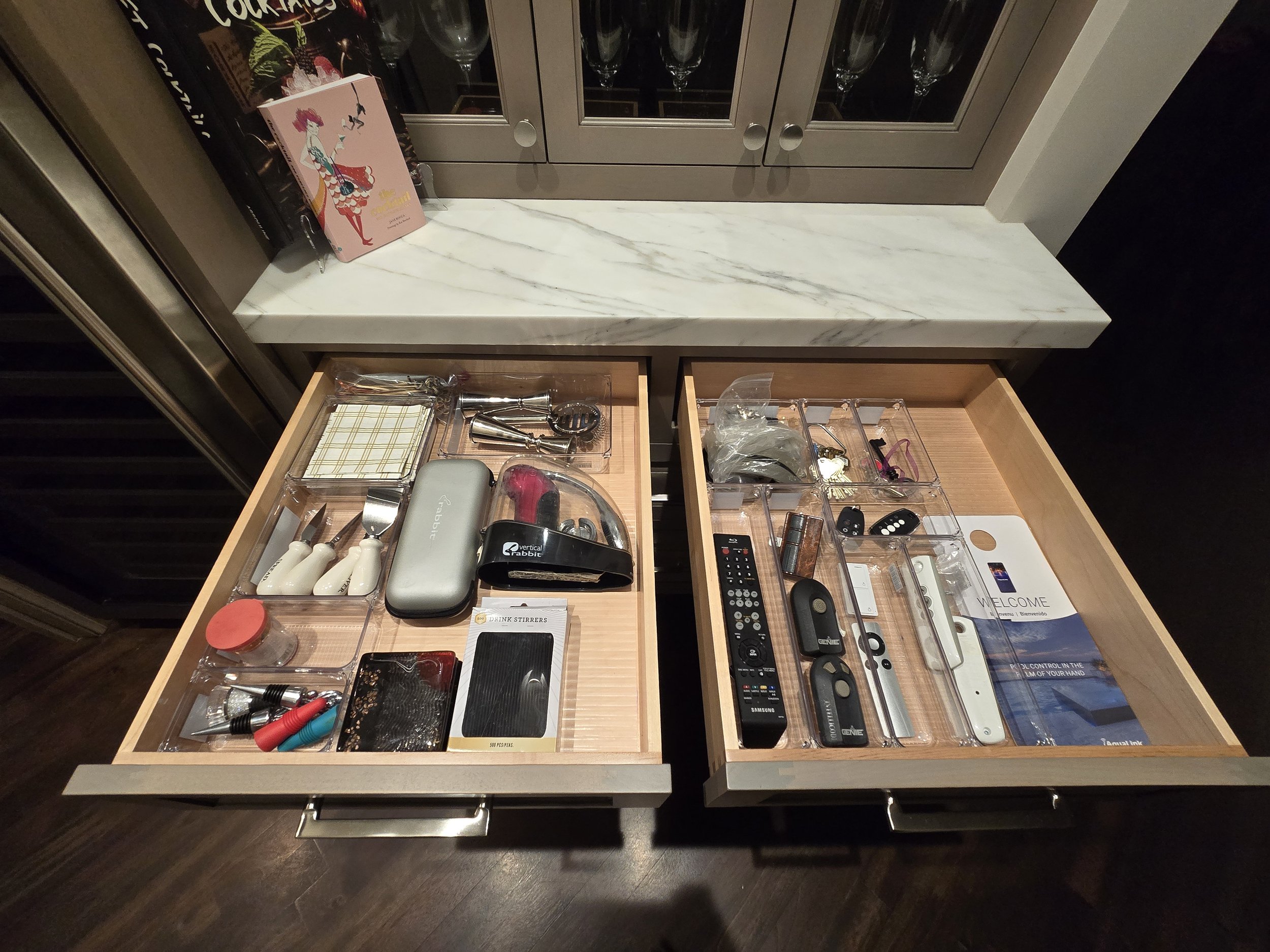 Open kitchen drawers with various household items, including remote controls, tools, batteries, cosmetics, and personal accessories.
