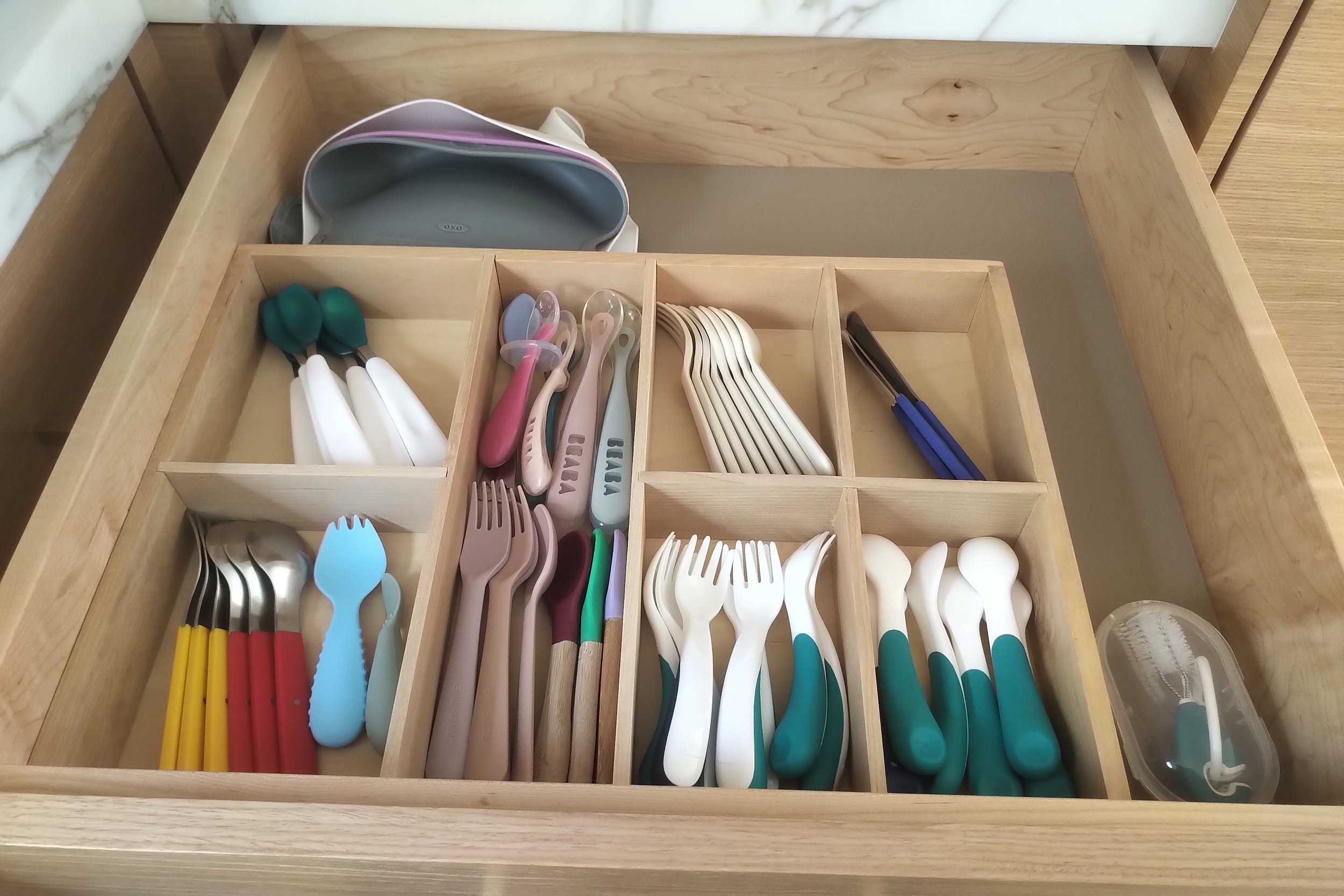 Wooden cutlery drawer organized with colorful utensils, including forks, spoons, and knives.
