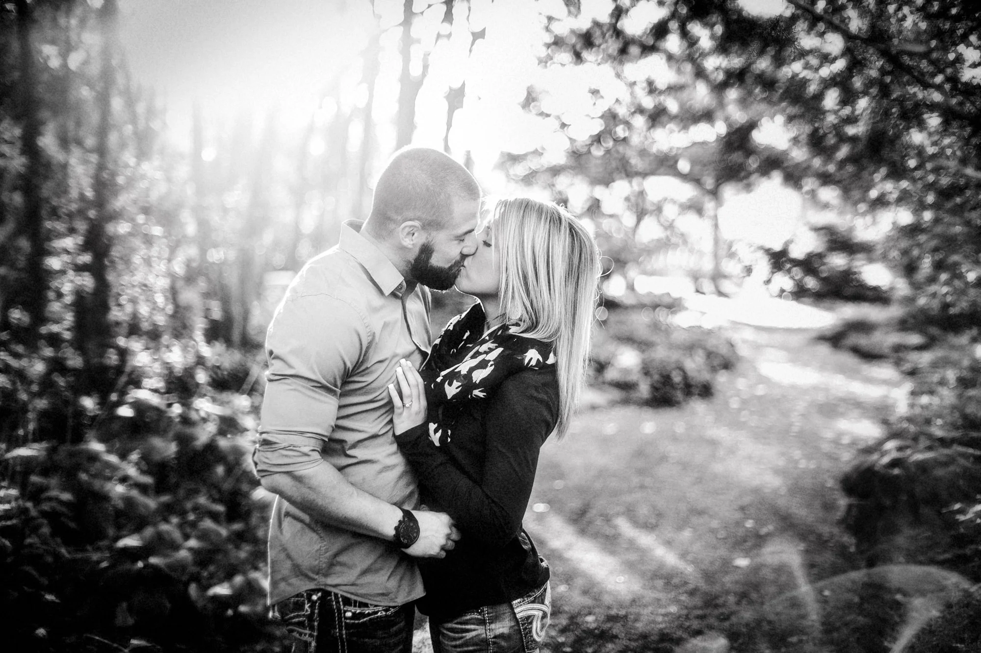 A young couple enjoys a kiss with the sun setting behind them in a forrest trail, in this outdoor photography session by Lauren Guiffré, a Boise Idaho couples photographer.
