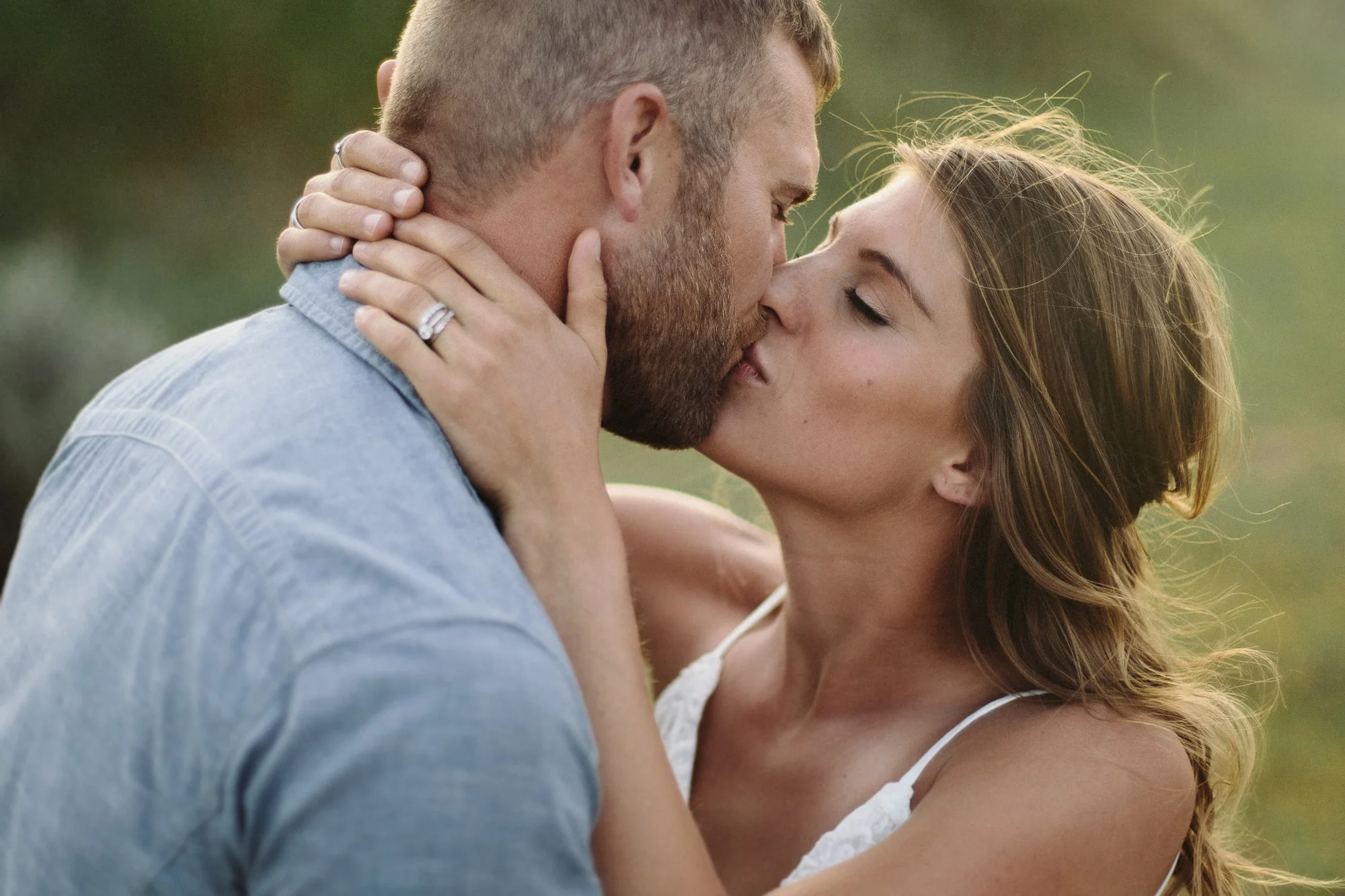 A young couple enjoys a tender kiss as she wraps her hands around his neck in an outdoor couples photography session.