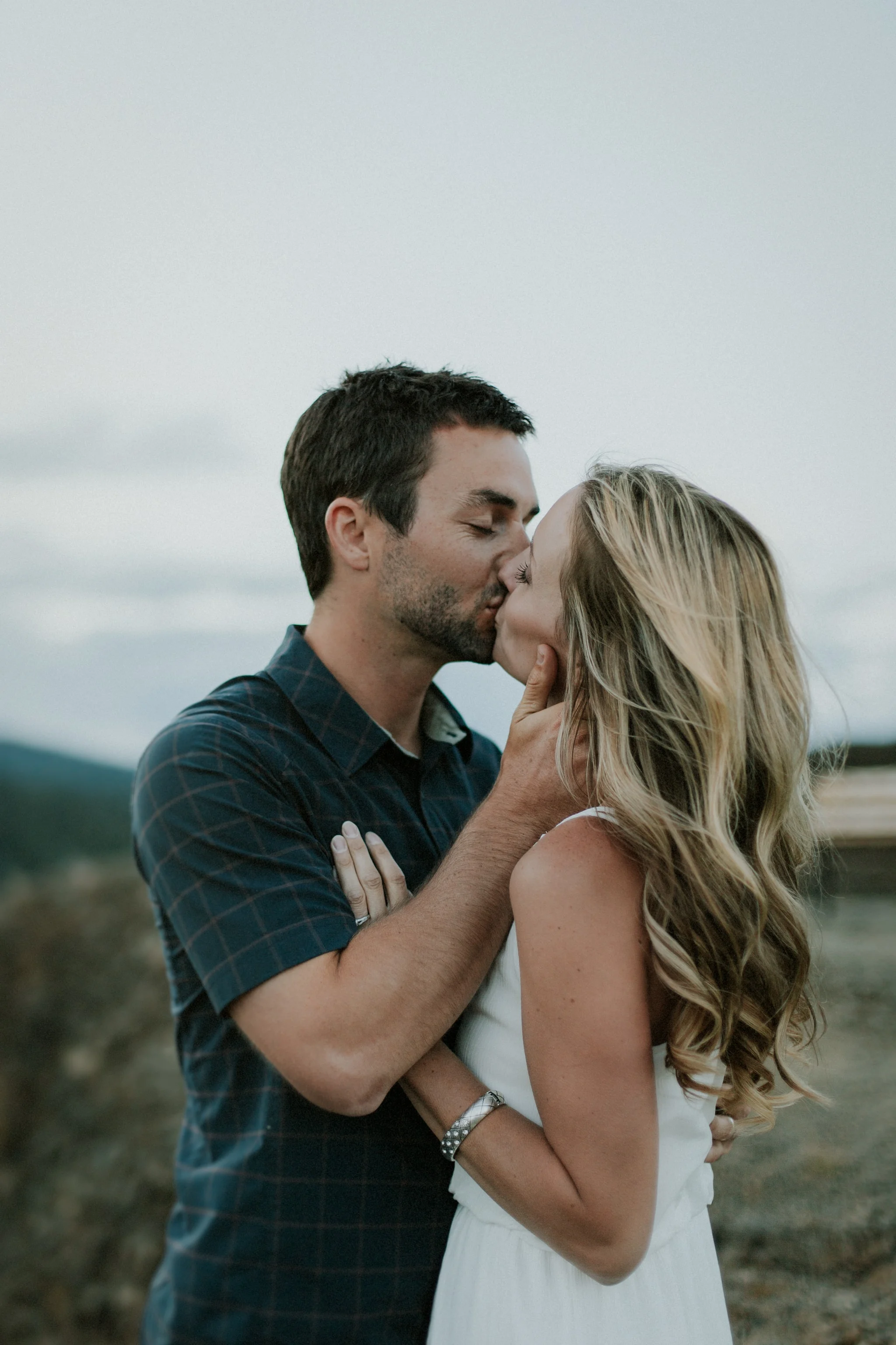 A photograph of a young couple kissing. He tenderly takes her head in his hands while she rests her hands on his chest in a couples photography session.