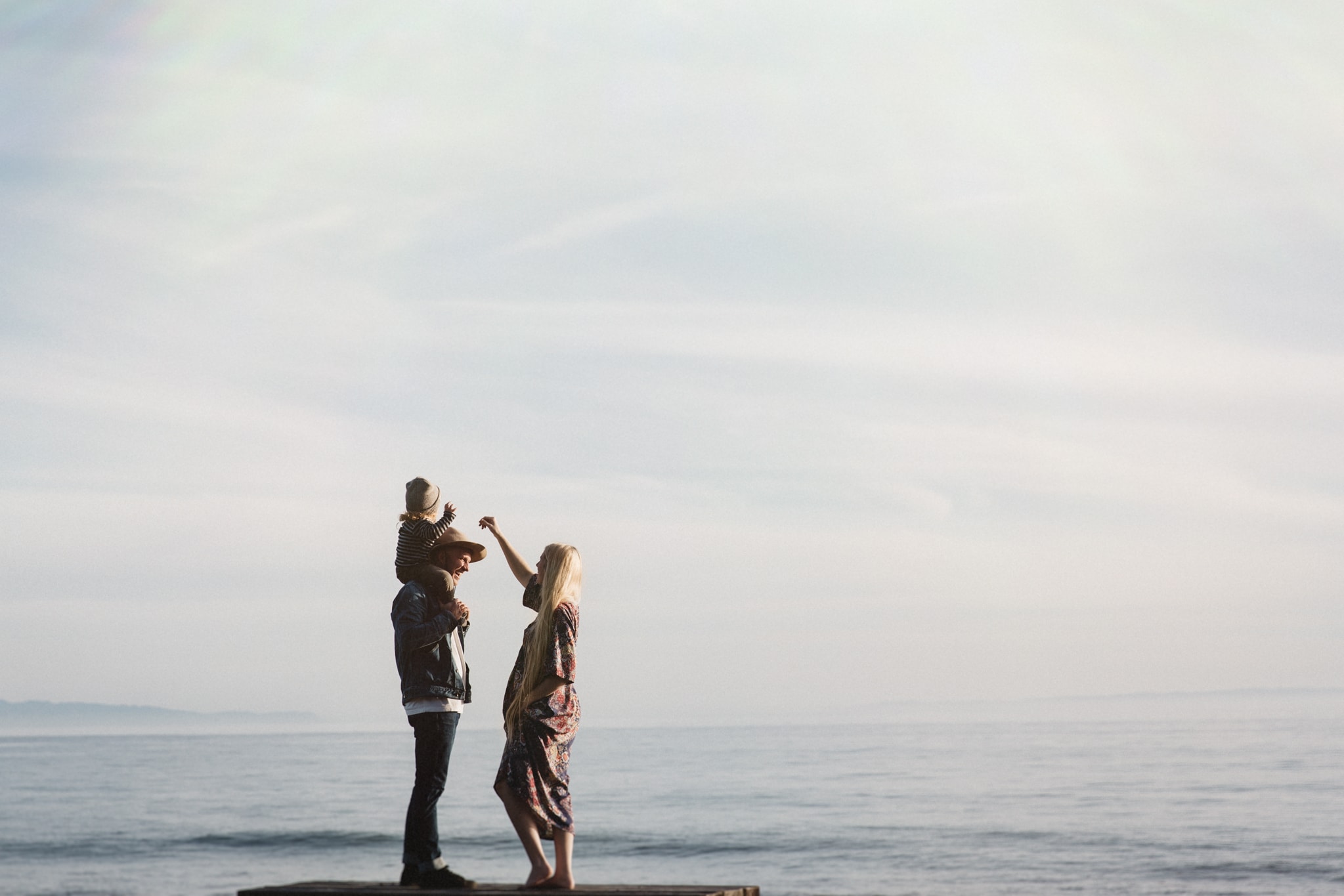 A photograph of a mother-to-be with her family, standing in front of the water, in this outdoor maternity photography session by Lauren Giuffré Photography, a Boise Idaho maternity photographer.
