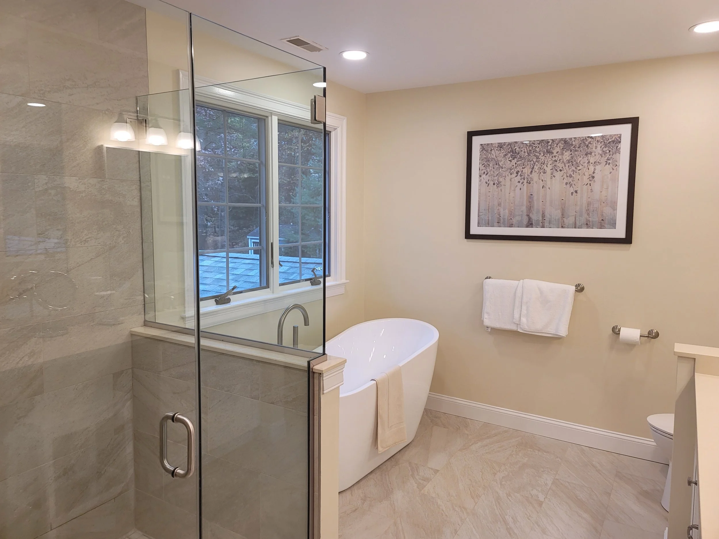Primary bathroom in Stow MA with freestanding soaking tub, glass shower enclosure, and quartz half wall