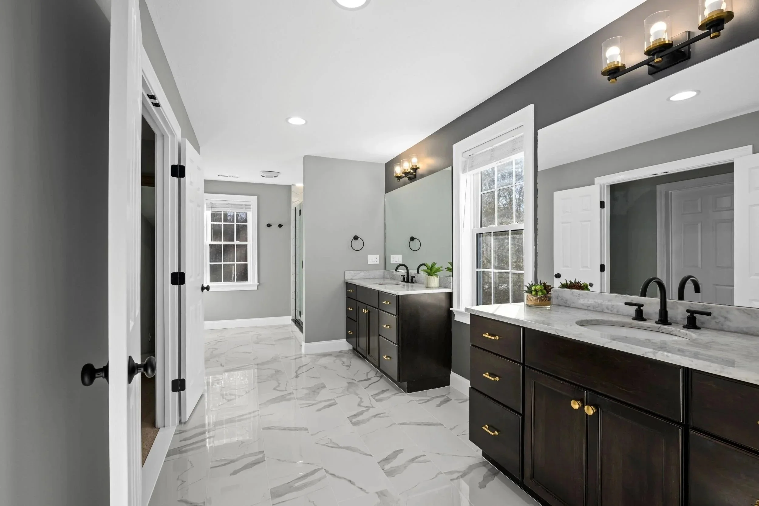 View into a Boxborough MA master bathroom featuring a double vanity with quartz countertops, matte black fixtures, and marble-look tile flooring
