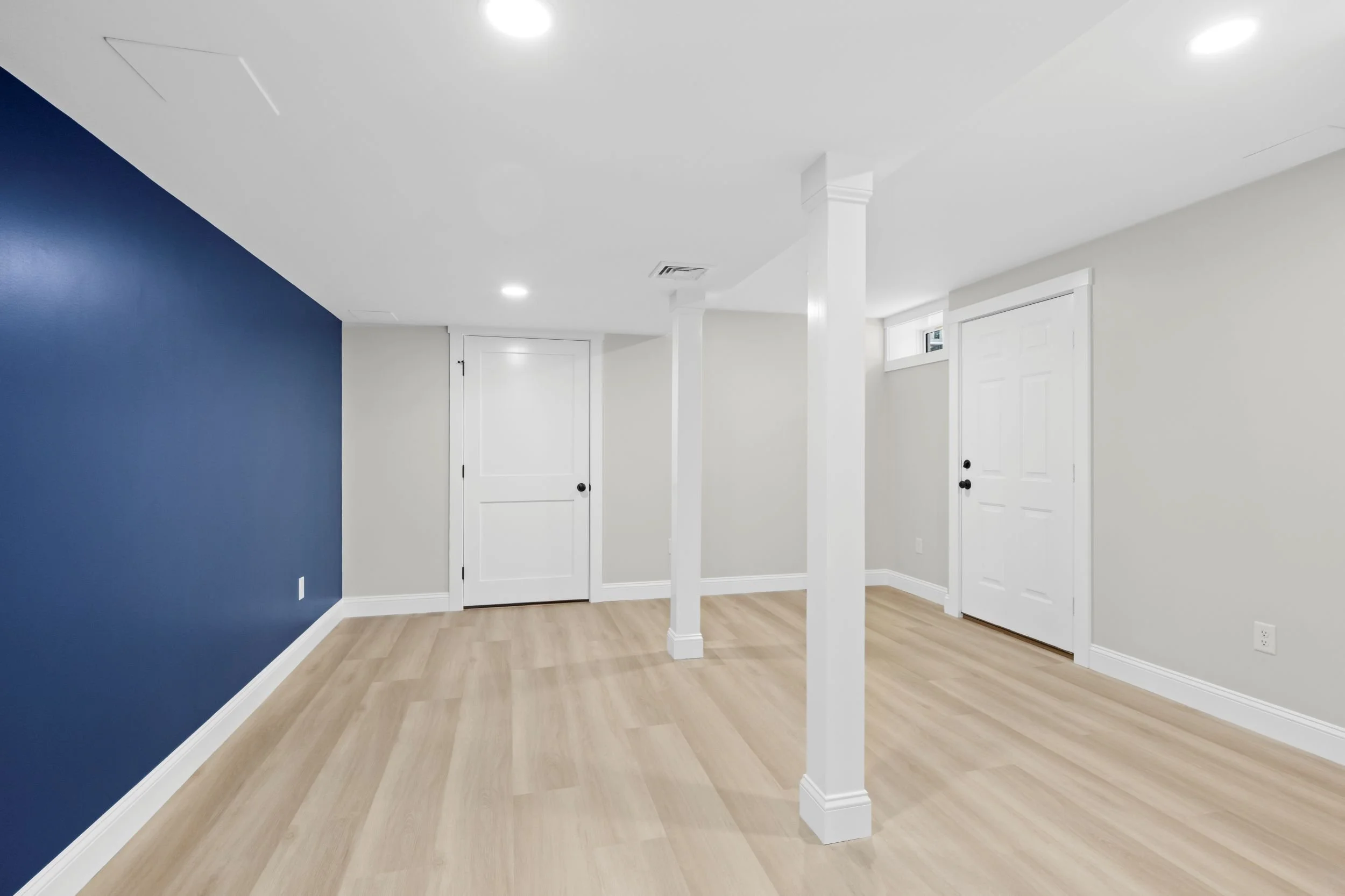 Reverse angle view of a finished basement living area in Boxborough, MA, showing the transition from the navy blue media room to the bright, open-concept family space.