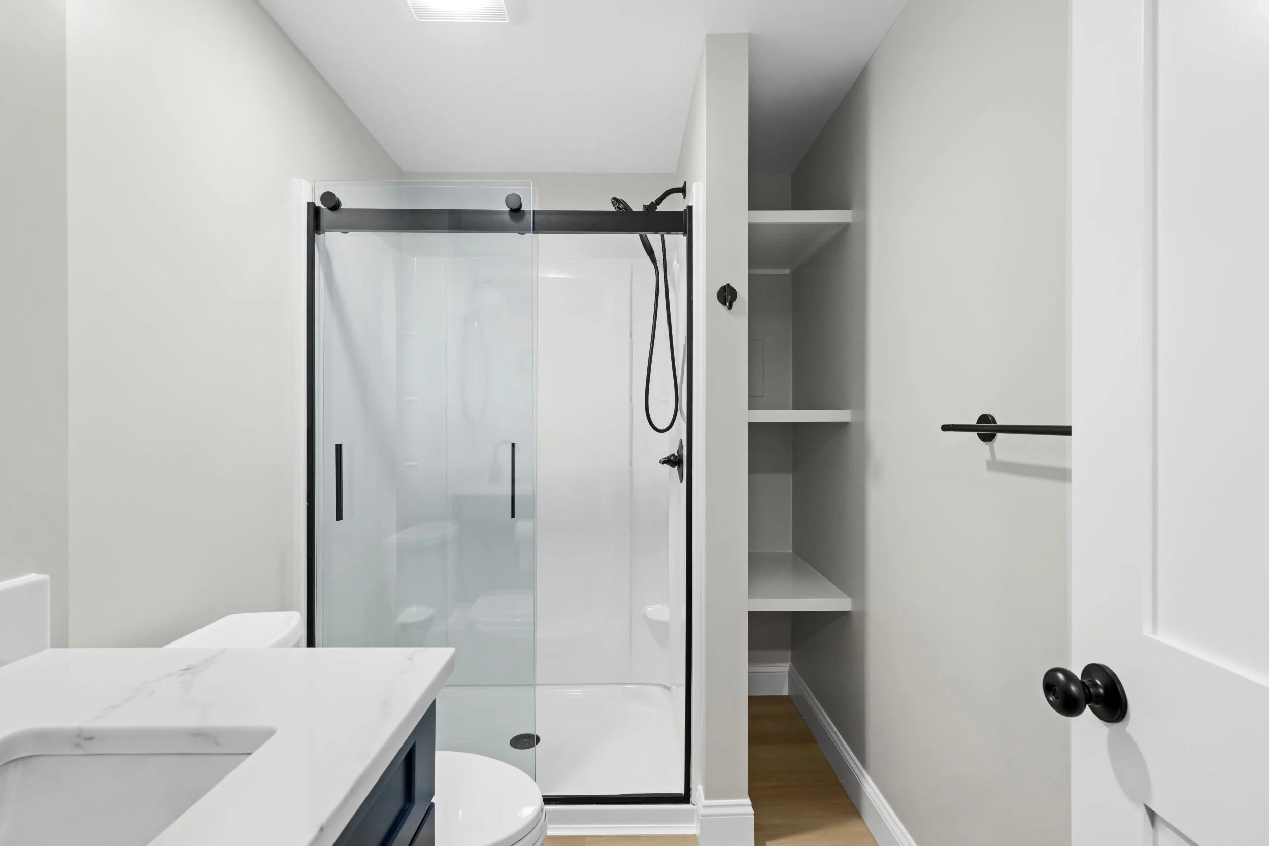 Clean and modern walk-in shower with a semi-frameless sliding glass door and integrated shelving in a Boxborough, MA basement remodel.