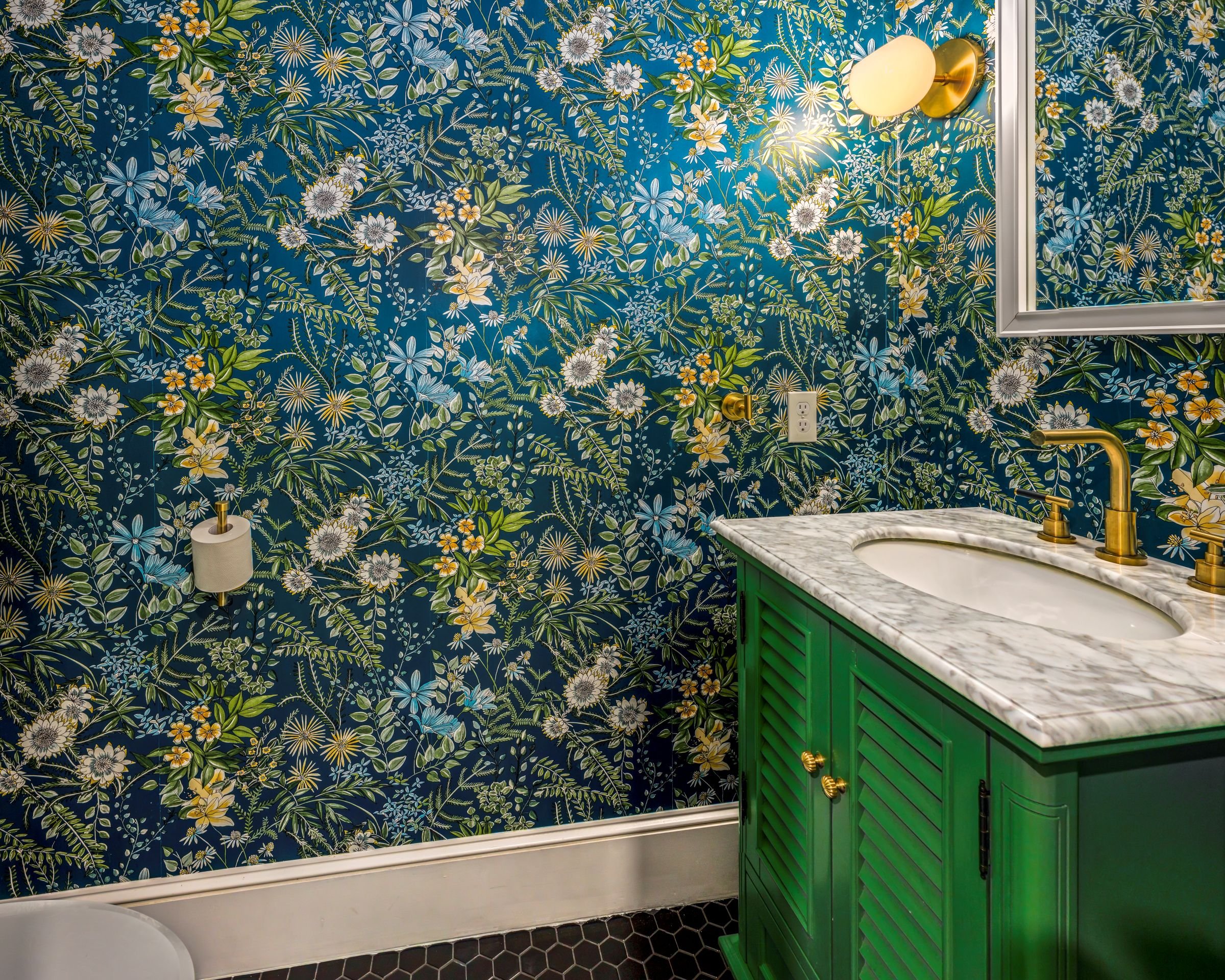 Close-up view of the green vanity, marble countertop, and brass faucet set against bold floral wallpaper in a Worcester, MA powder room remodel.