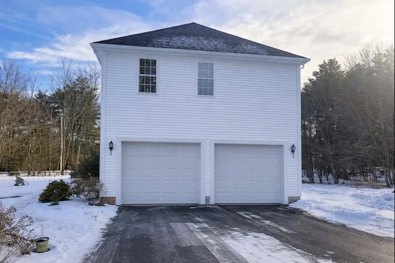 Two-story home addition in Hopkinton, MA with matching vinyl siding, new roofing, and double garage doors