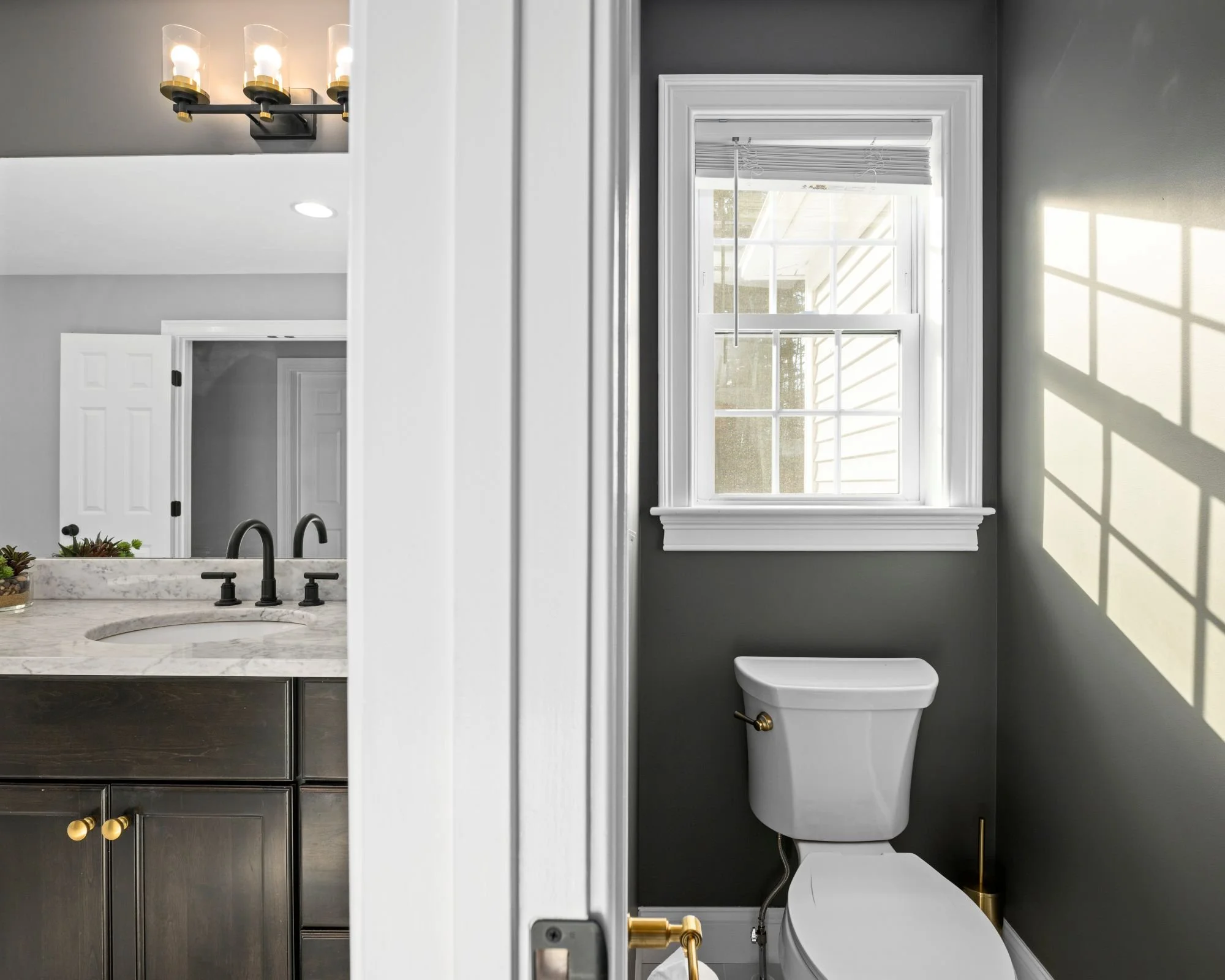 Toilet area with window and natural light adjacent to dark vanity with marble countertop in a Boxborough MA master bathroom remodel