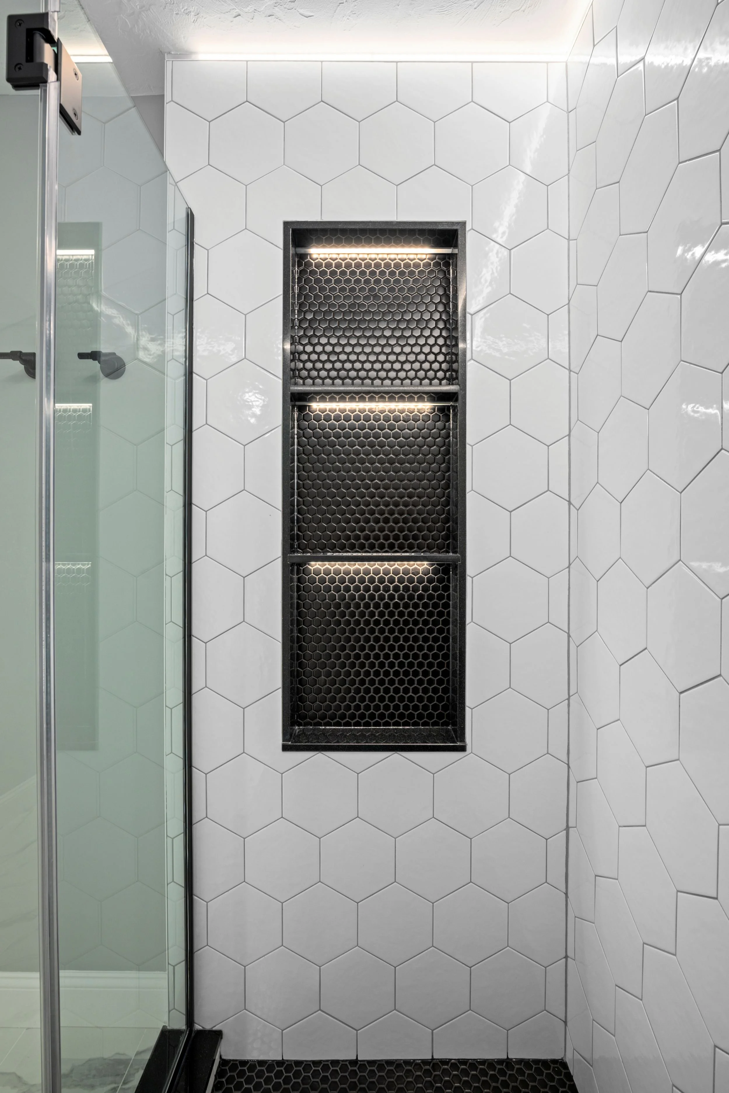 White hex tile shower walls with an LED-lit black hex tile niche and frameless glass panel in a Boxborough MA master bathroom remodel