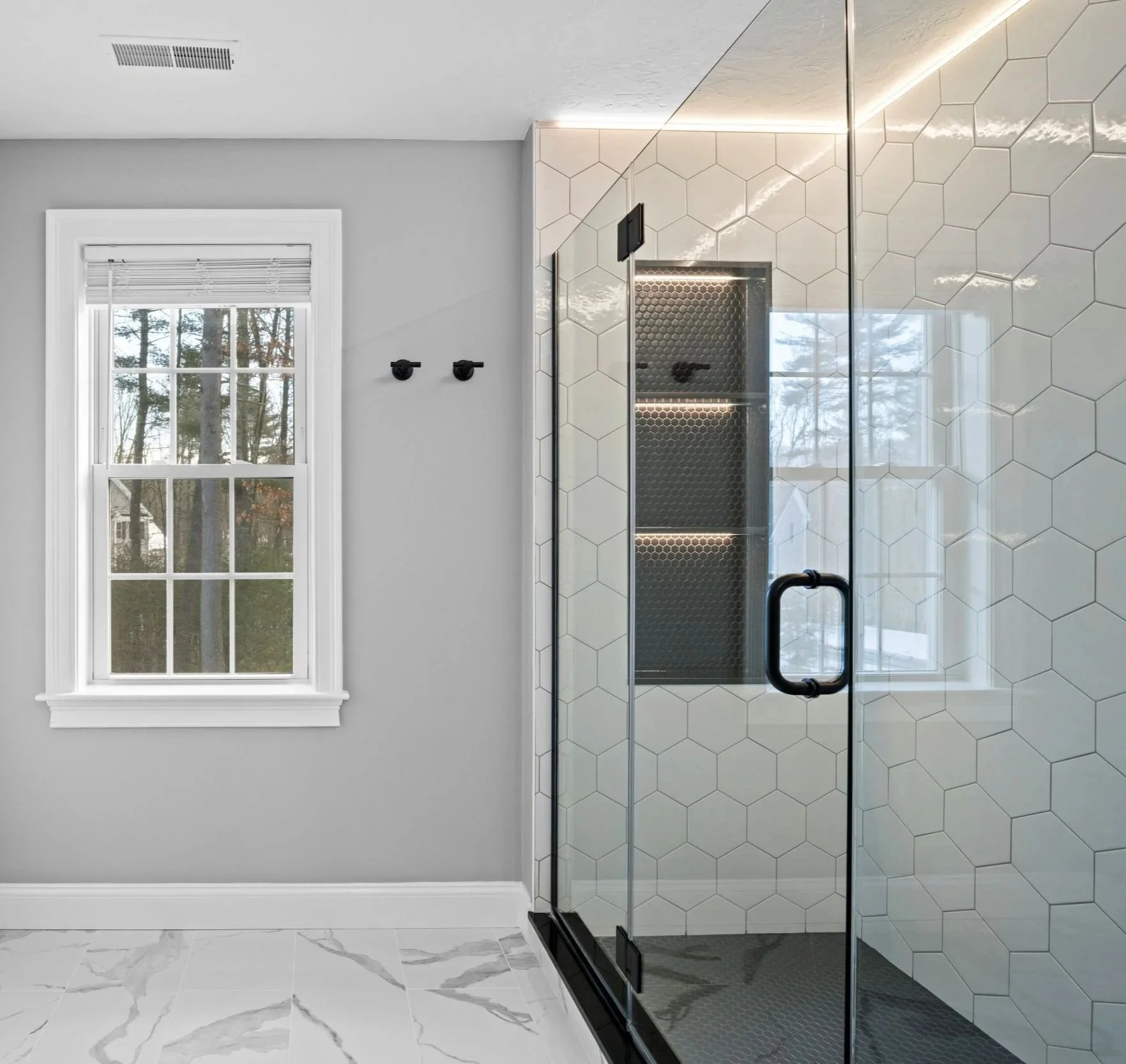 Natural light from the window brightens a master bathroom with marble-look tile floors and a frameless glass walk-in shower in Boxborough MA