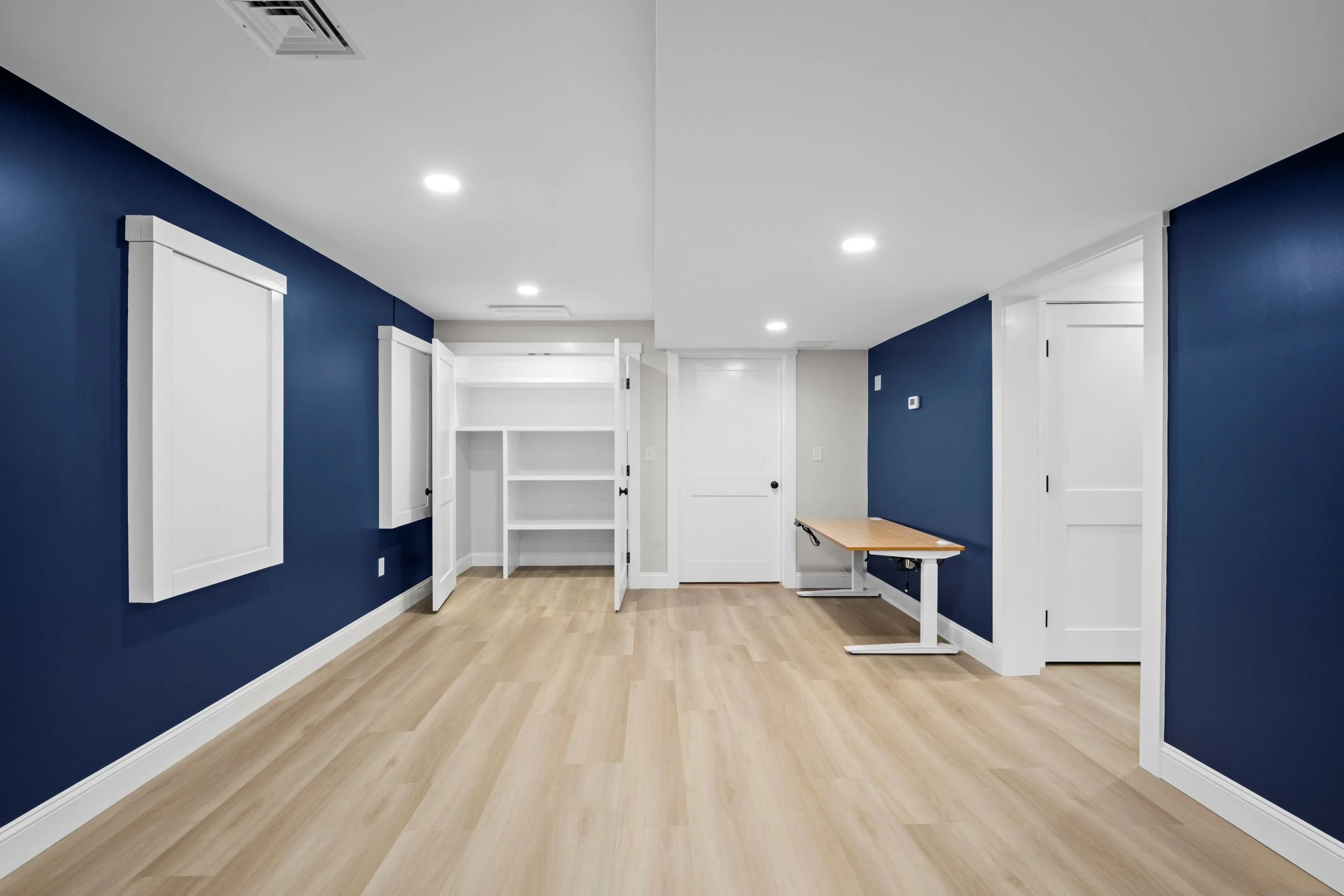 Basement renovation in Boxborough, MA showcasing a built-in office workstation and organized storage closet in the main living space.