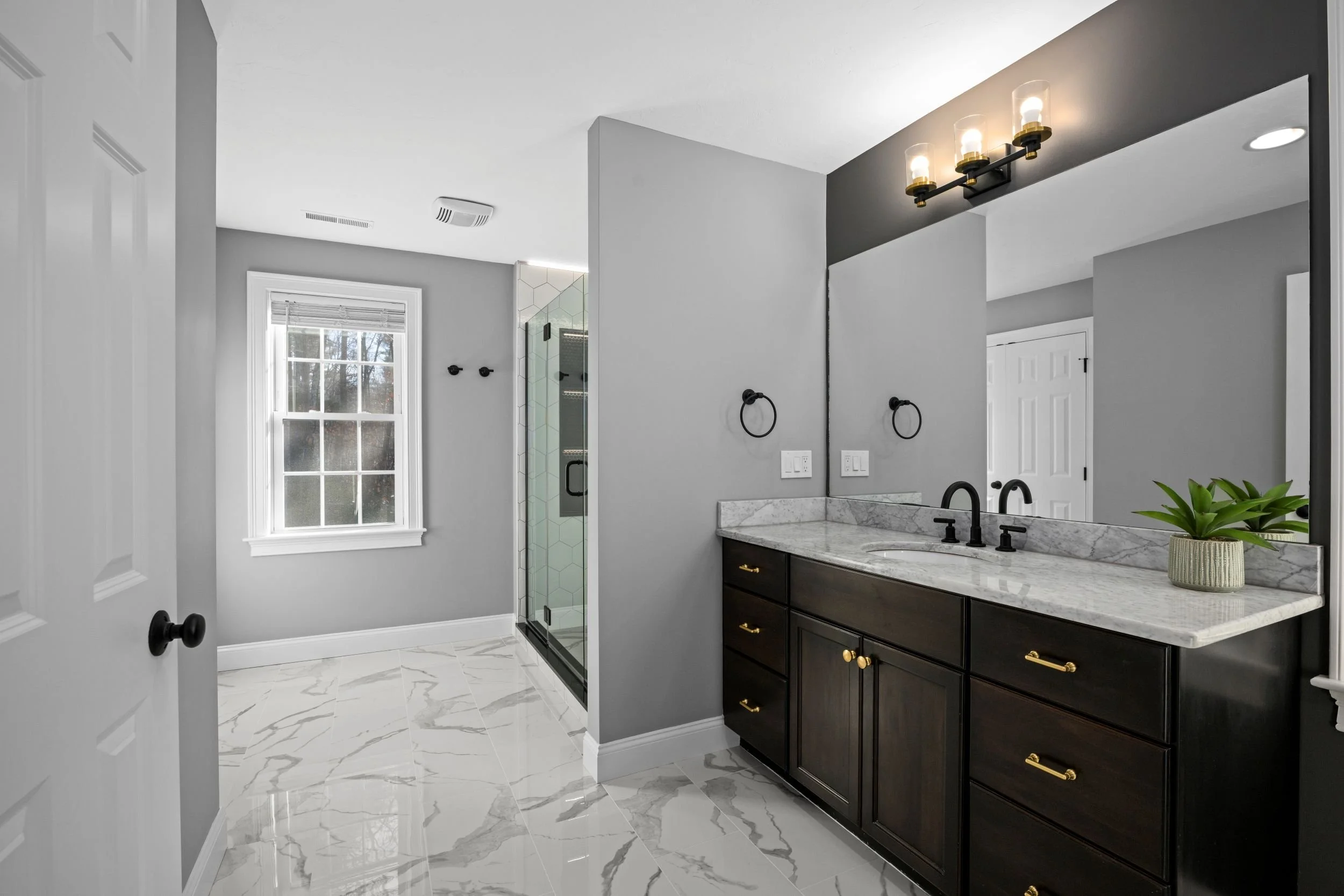 Modern bathroom remodel in Boxborough, MA featuring a dark wood double vanity, marble-look tile flooring, and a glass-enclosed walk-in shower.