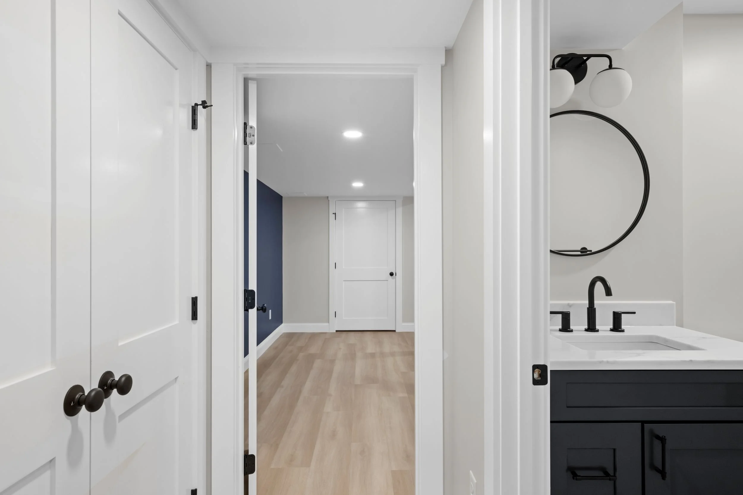 Modern basement bathroom vanity in Boxborough, MA, featuring charcoal shaker cabinets, quartz countertops, and a round matte black mirror.