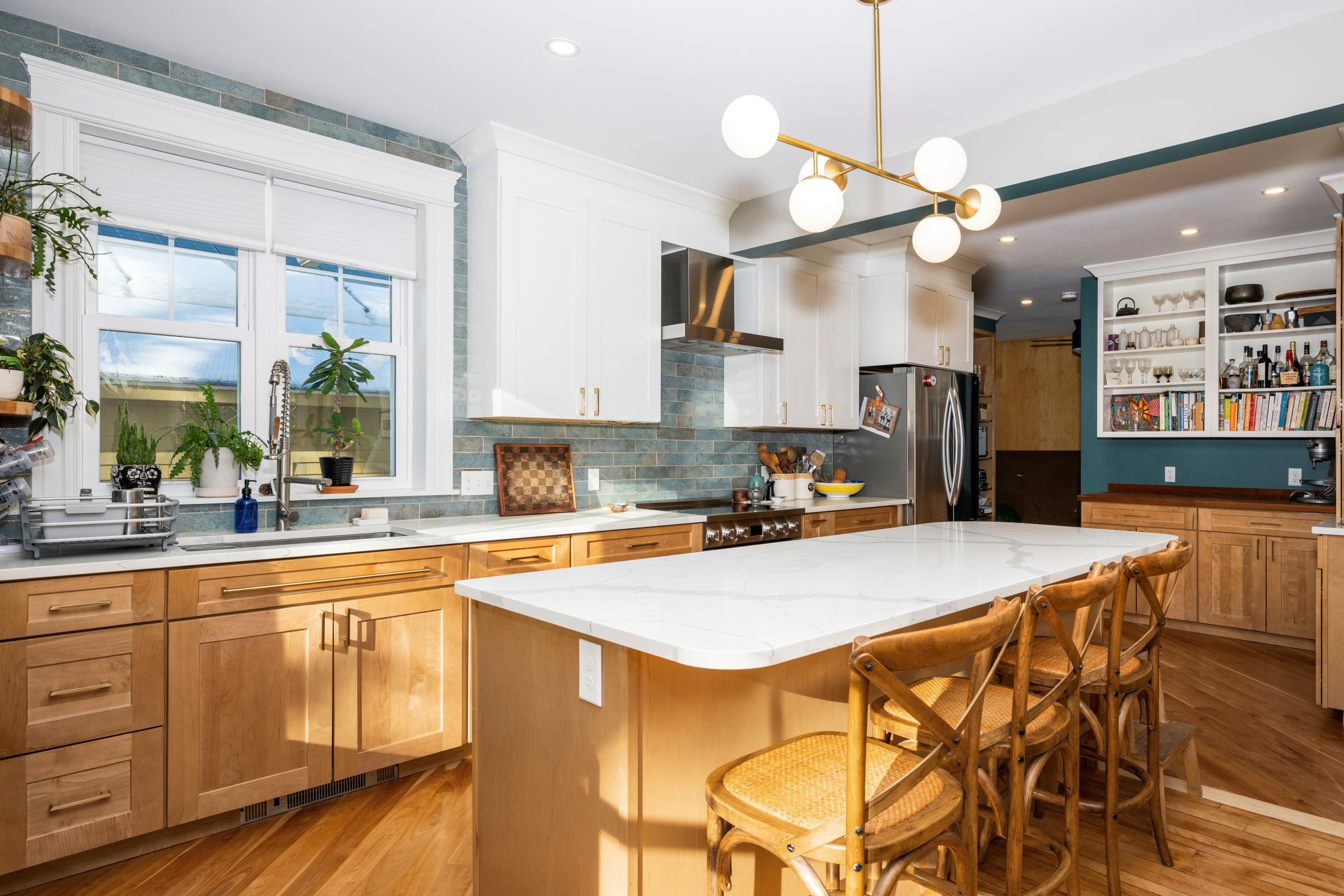 Kitchen island and dining area in a Worcester MA remodel featuring Statuario Classic quartz countertops, natural wood island base, and white cabinetry with brass lighting.