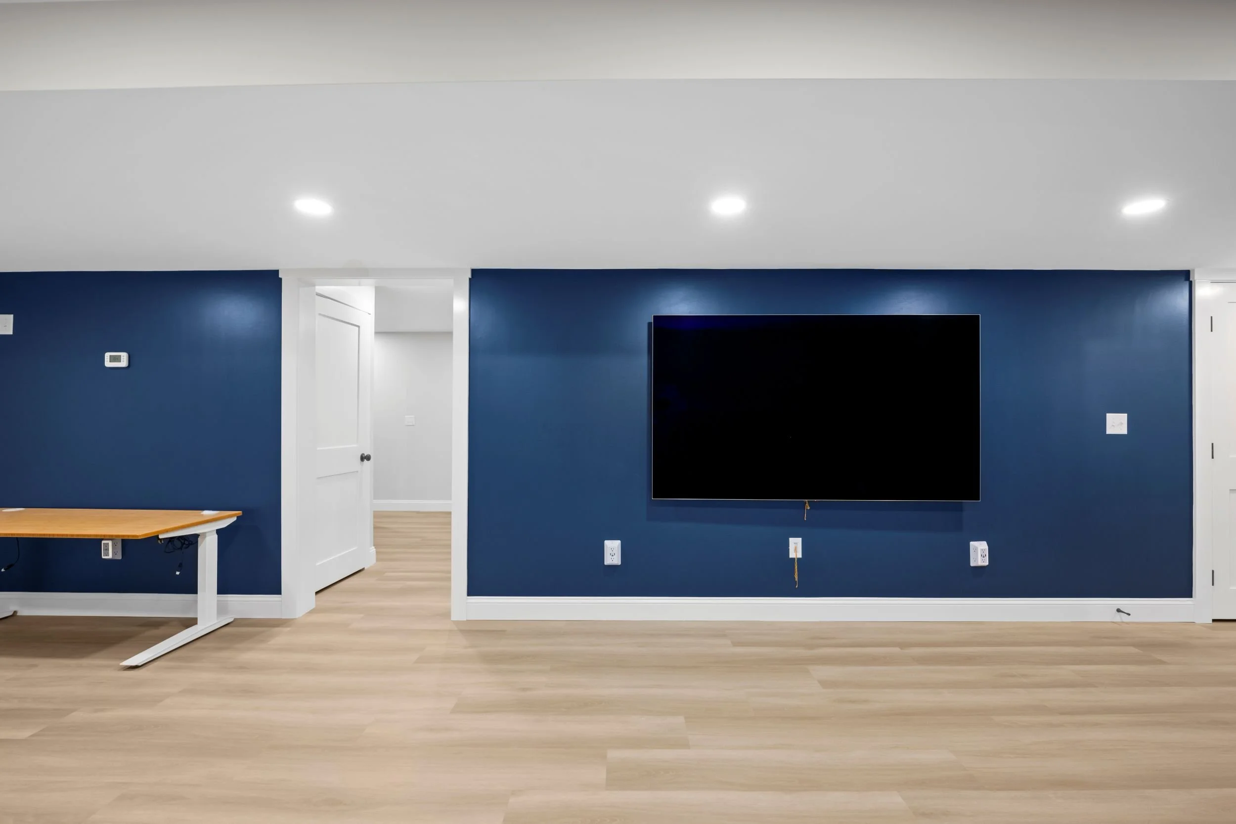 Modern basement media room with a large wall-mounted TV, deep blue accent walls, and luxury vinyl plank flooring in Boxborough, MA.