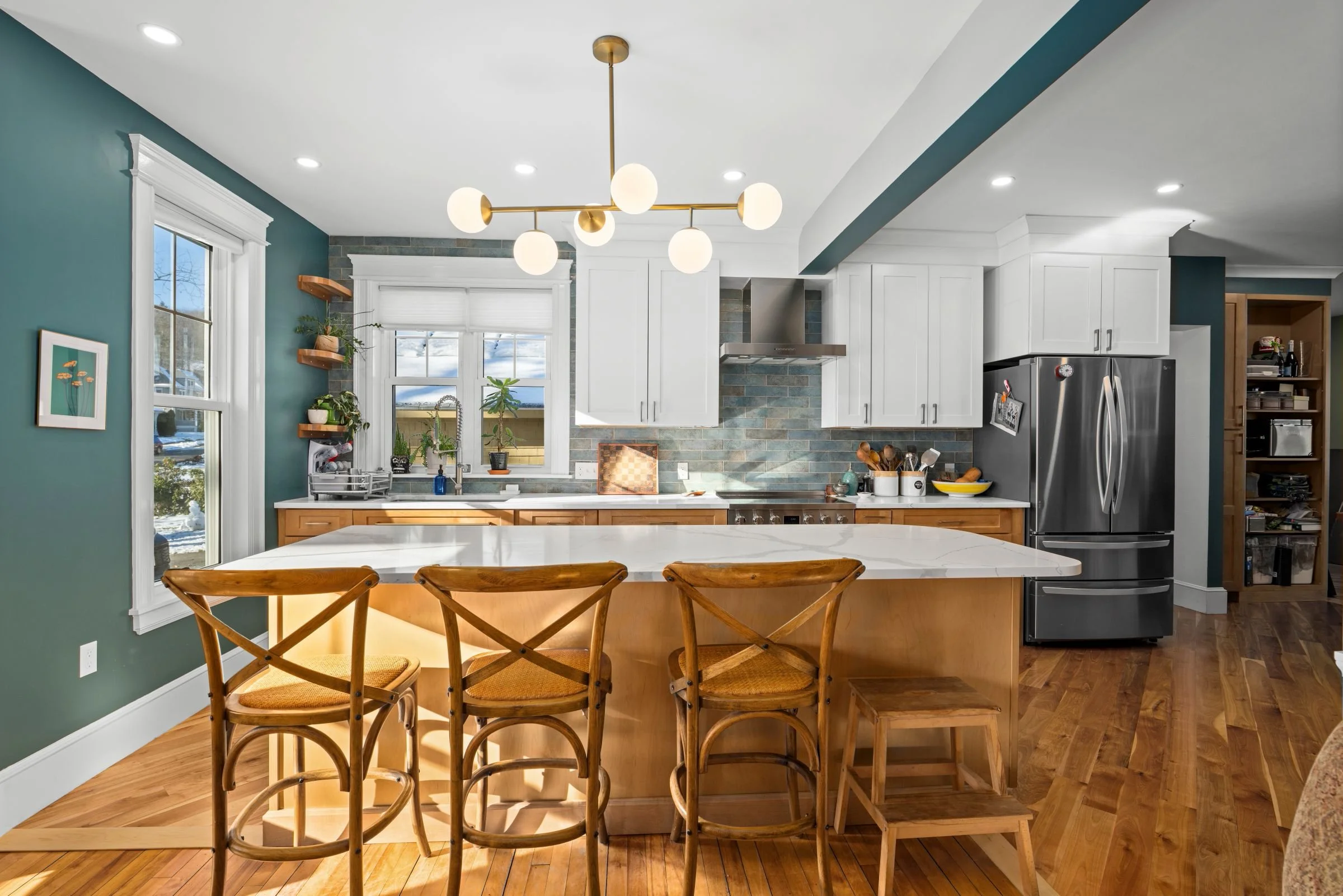 Opposite angle of Worcester MA kitchen remodel featuring island seating, quartz countertops, stainless steel appliances, and Kalay Green backsplash.