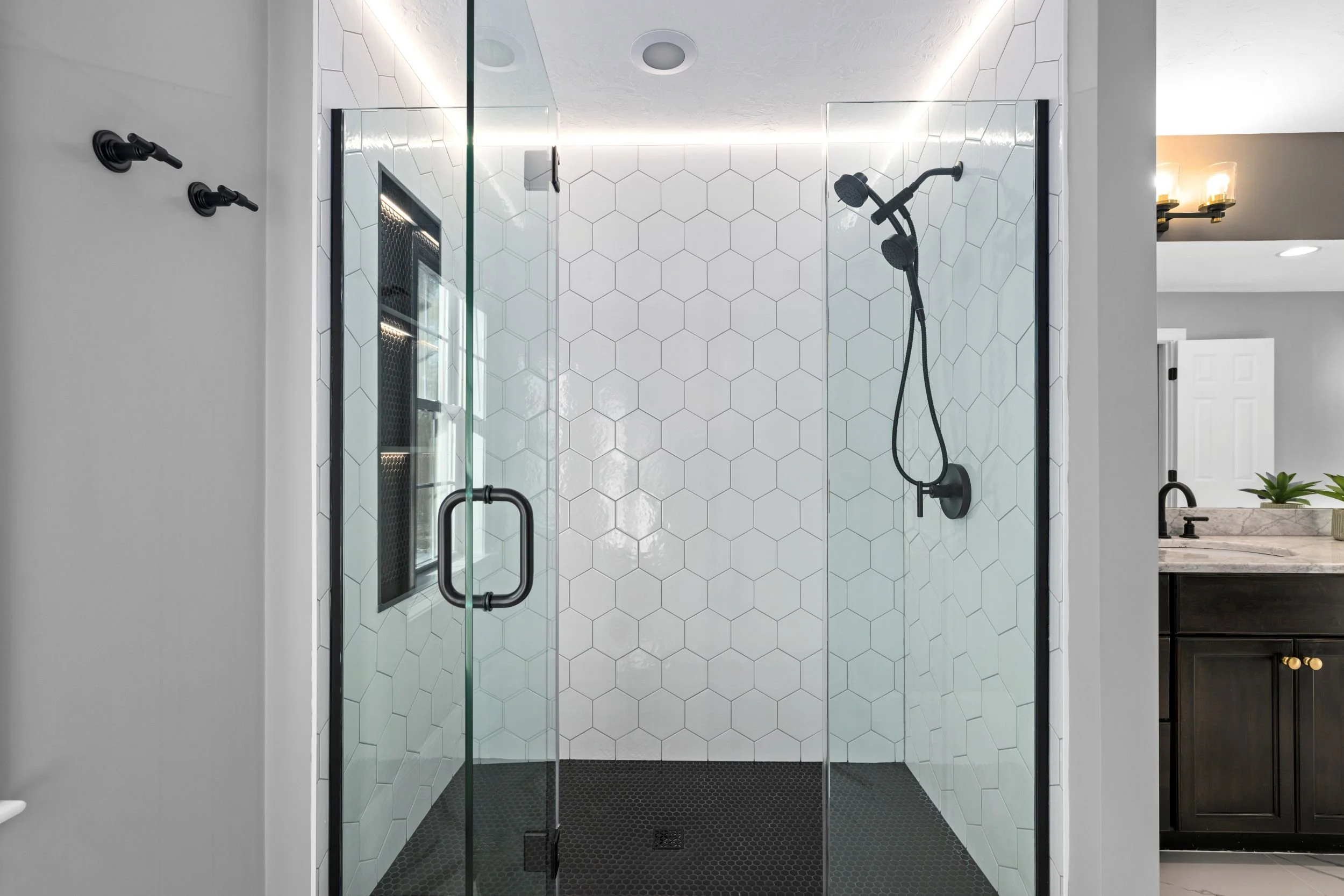 Walk-in shower with white hex tile walls, matte black fixtures, frameless glass door, and LED lighting in a Boxborough MA master bathroom remodel