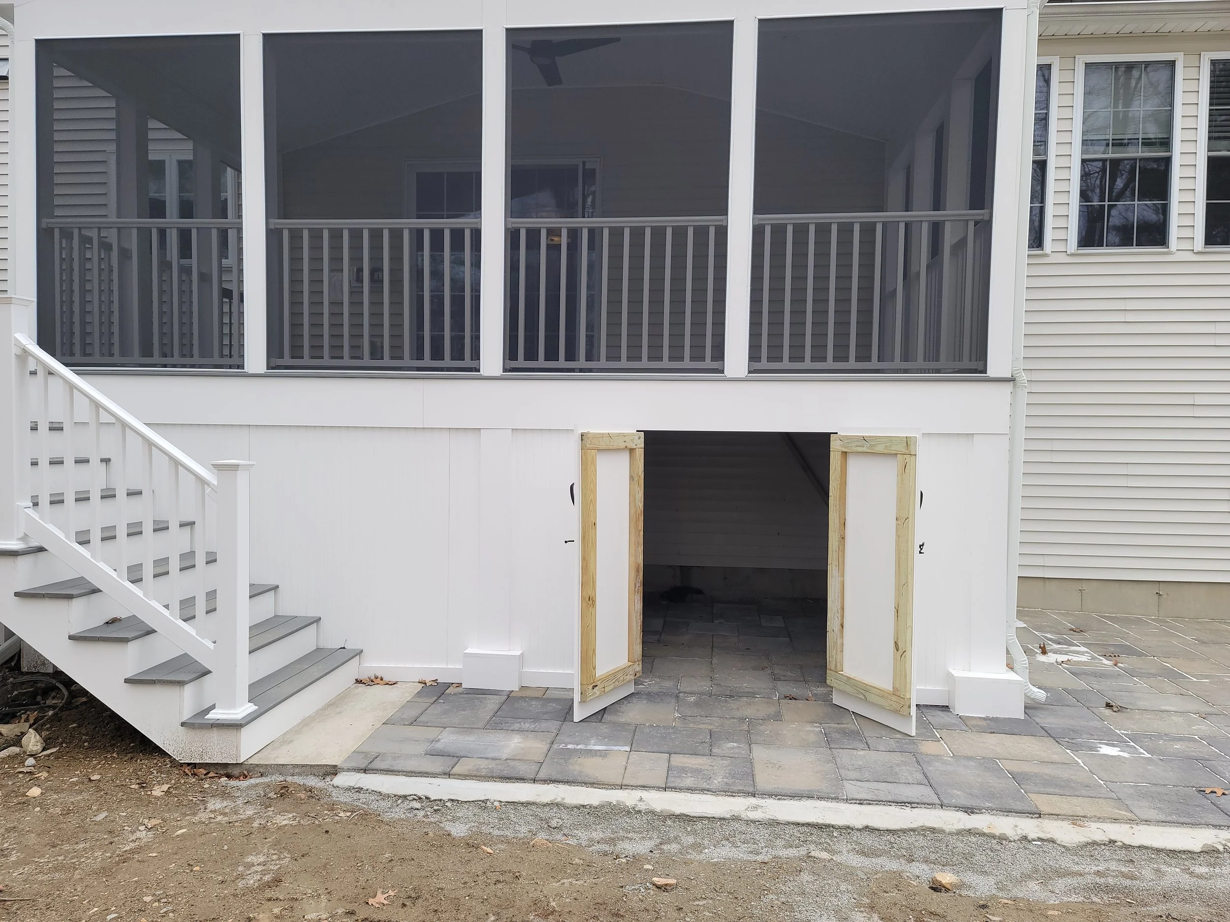 Under-deck storage area beneath three-season screen room with paver patio in Ashland MA
