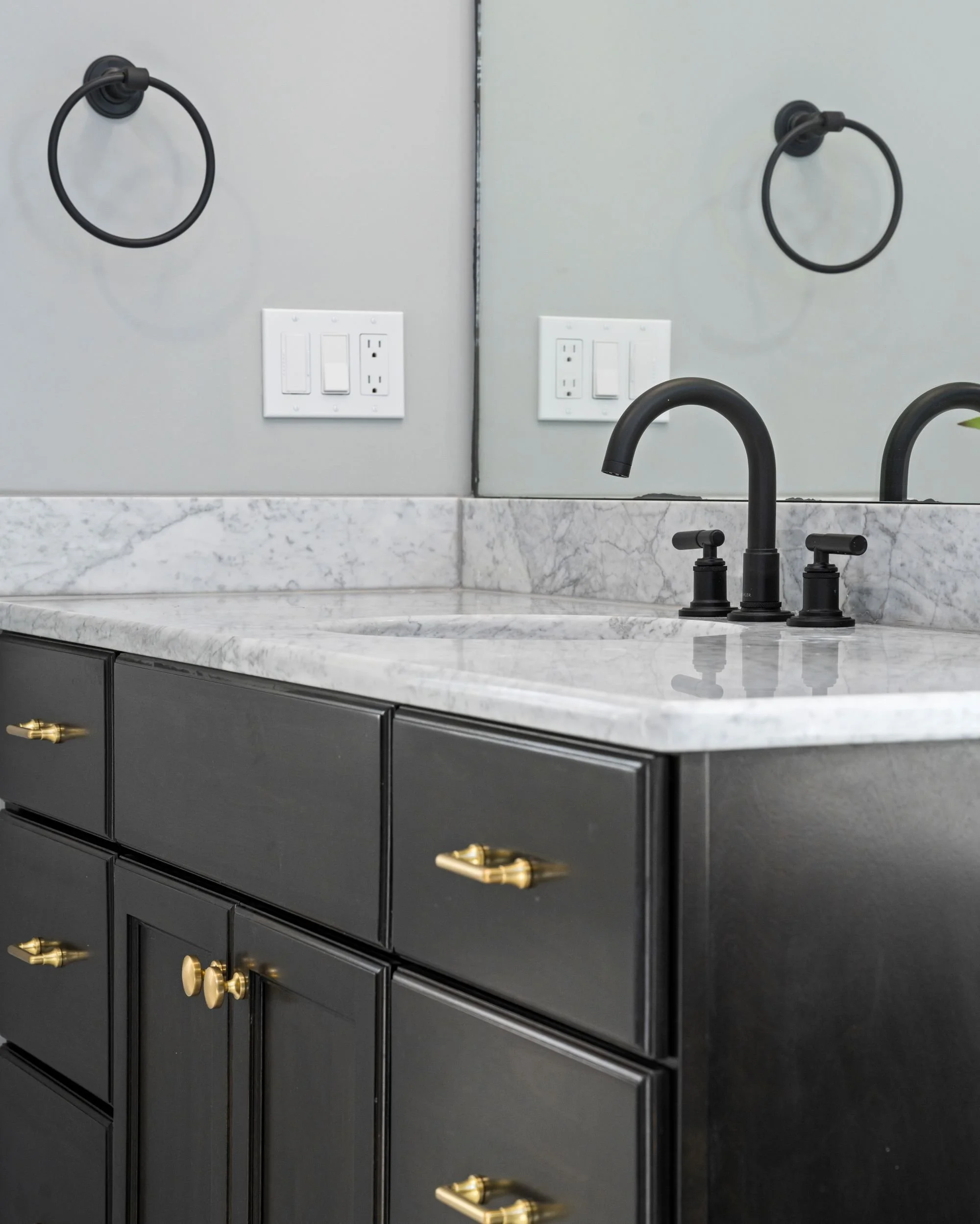 Matte black bathroom faucet on marble countertop with dark vanity cabinetry and brass hardware in a Boxborough MA master bathroom remodel