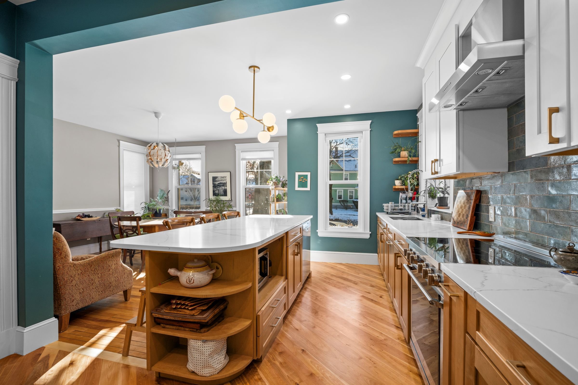 Opposite angle showing island seating, quartz countertops, stainless steel appliances, and the Kalay Green backsplash.