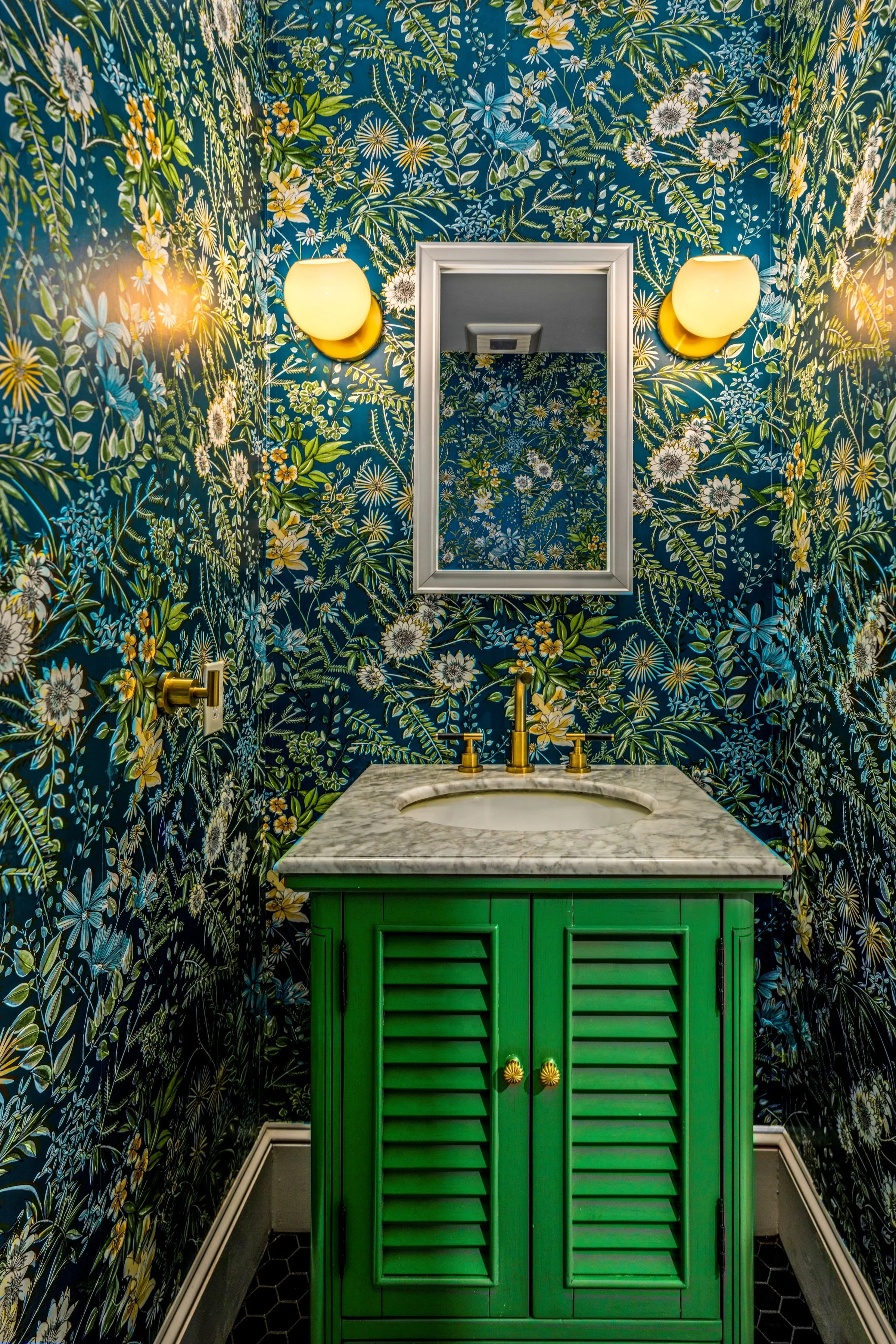 Powder room with bold floral wallpaper, a green vanity with marble countertop, brass fixtures, and warm sconce lighting in a Worcester, MA remodel.