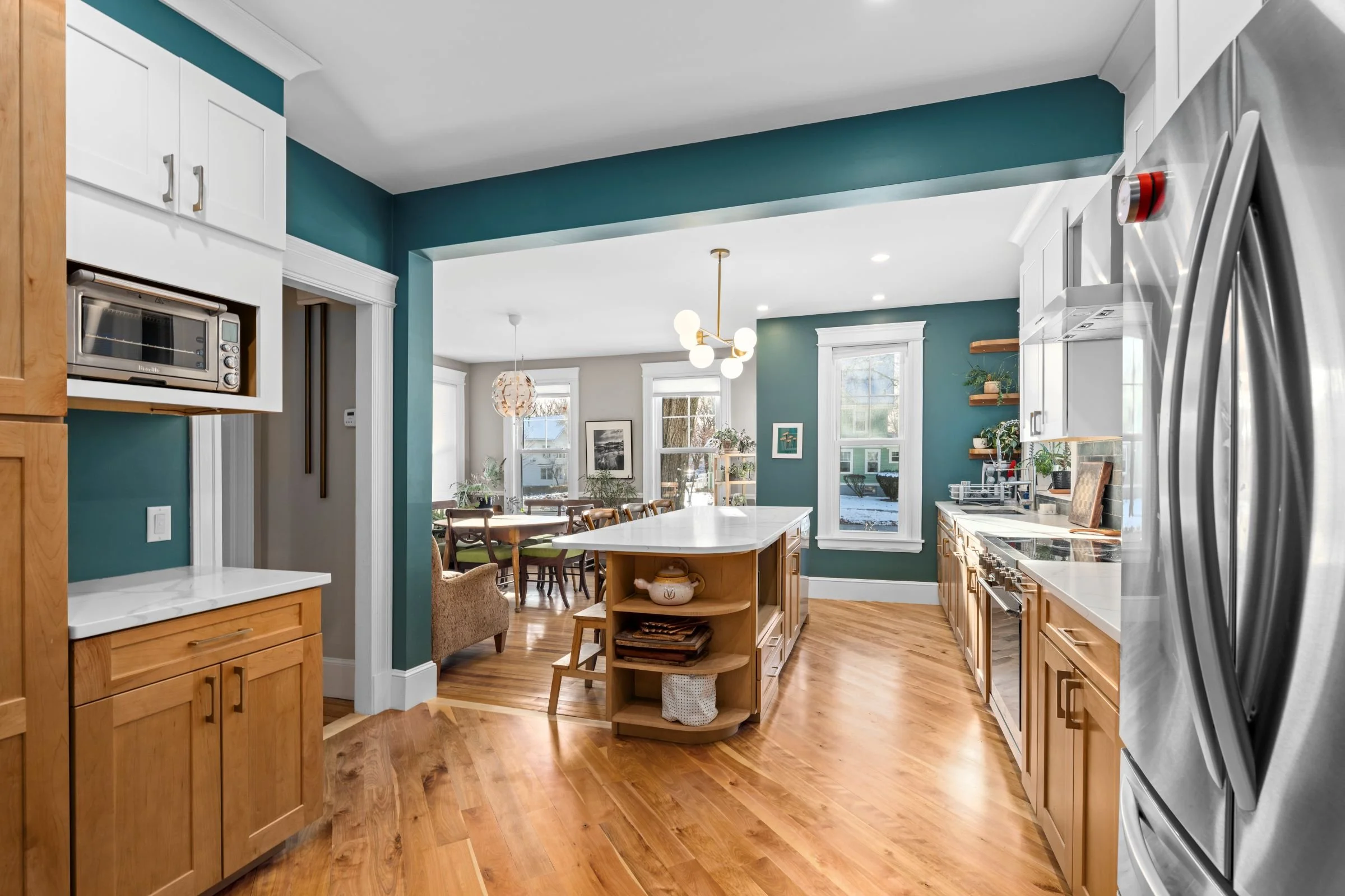 Kitchen island seating area in a Worcester MA remodel featuring natural wood cabinetry, Statuario Classic quartz countertops, and a Castel brass 6-globe linear pendant.