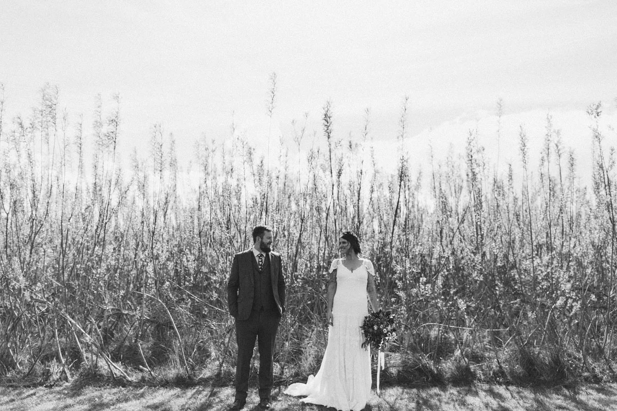 black and white wedding photo bride in white dress looking at groom lovingly tall grass in the background