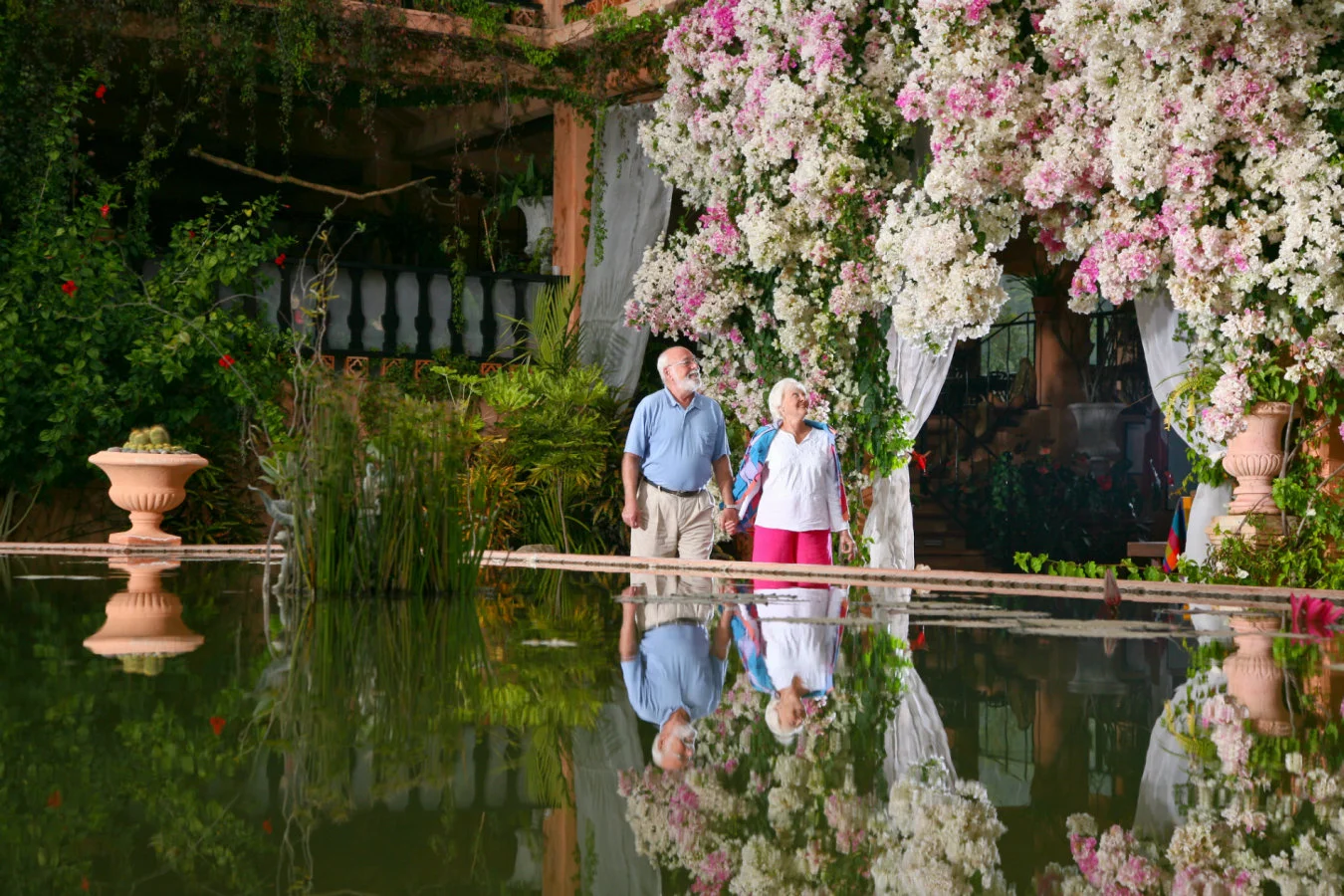 Elderly couple admiring flower arrangements near restaurant in botanical gardens.