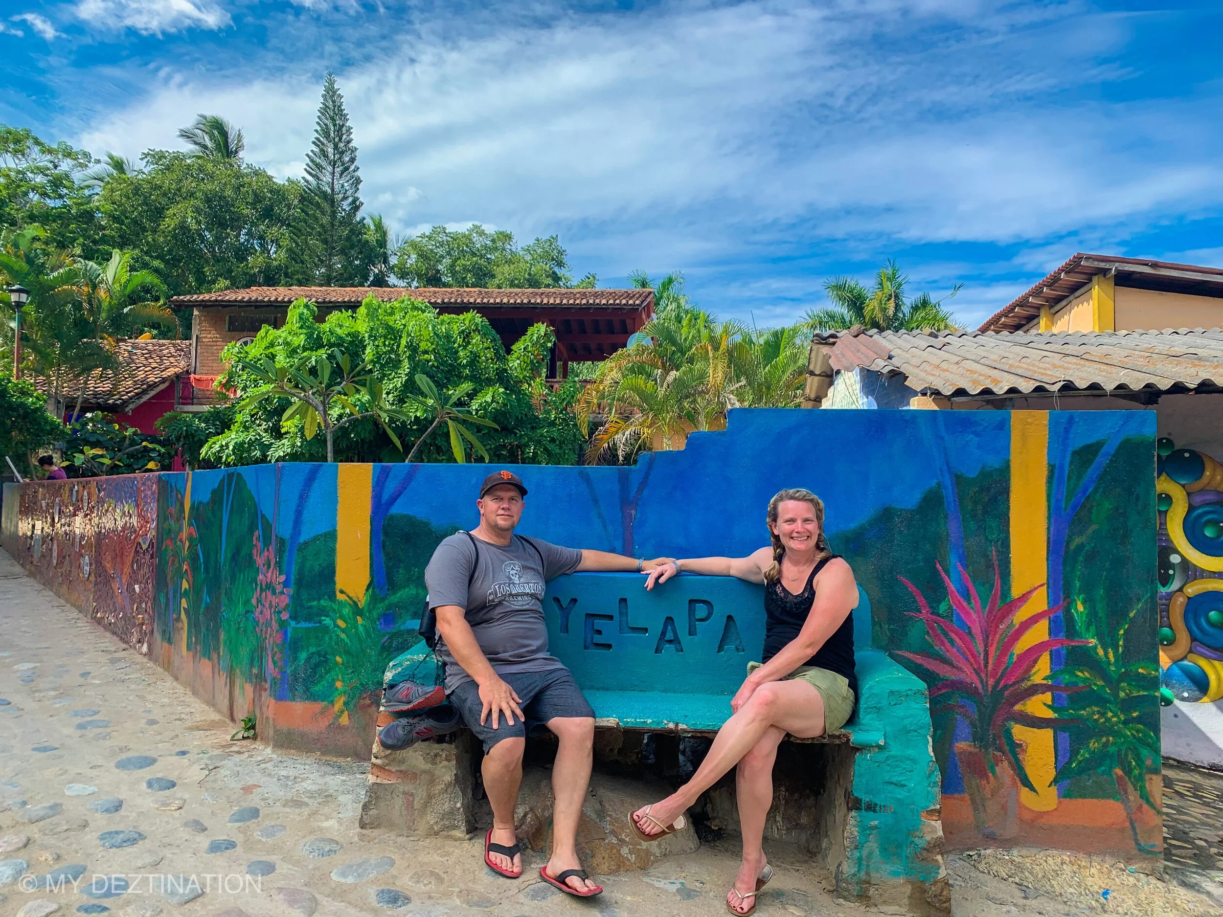 Guests sitting on a Yelapa bench with sign during My Deztination visit.