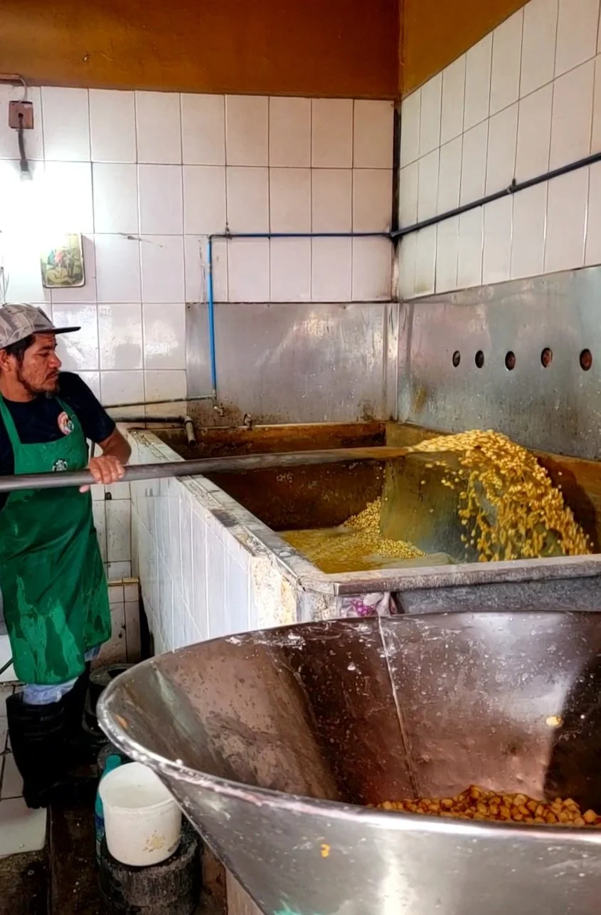 Local man in apron mixing food in large pot during My Deztination market tour.