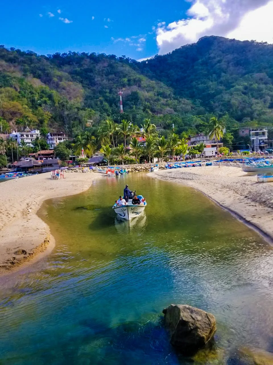 A traditional Mexican panga boat cruises from the river into the ocean, with Puerto Vallarta’s mountains in the background—set off on a private Los Arcos snorkeling adventure with My Deztination.