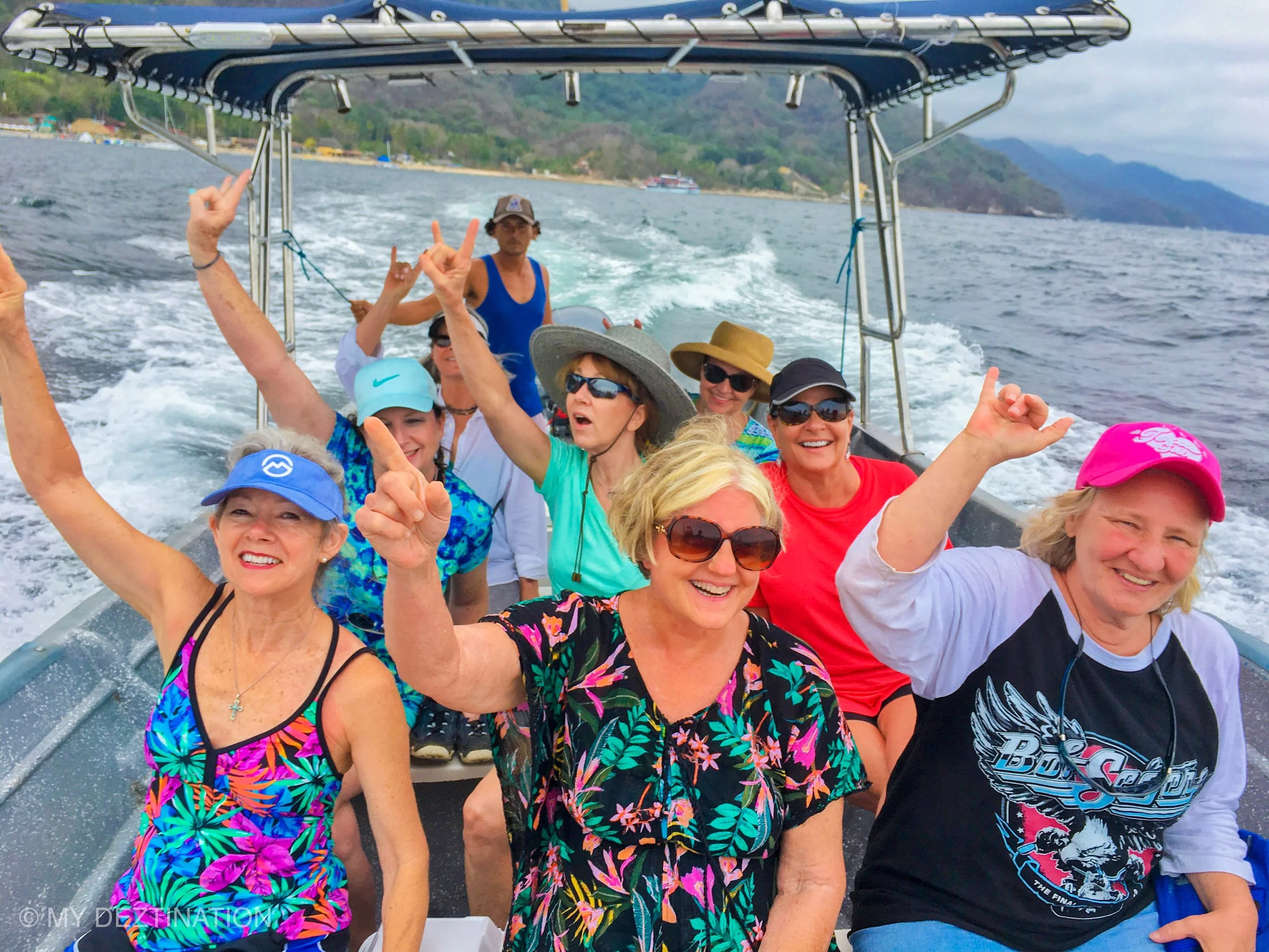 Group on boat speeding across bay with hands raised, My Deztination adventure.