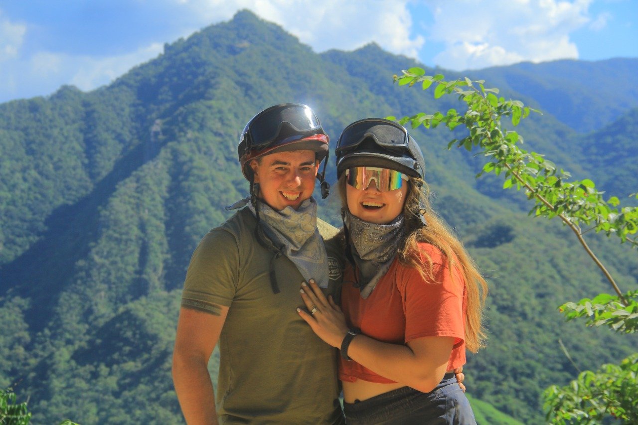 Couple smiling with helmets and mountain backdrop on My Deztination.