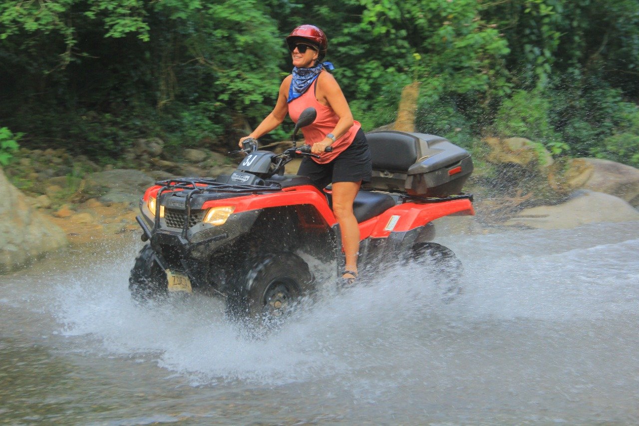 Guest standing on ATV riding through water with My Deztination.