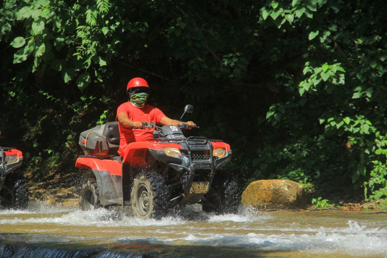 Guest with bandana driving through water on ATV, My Deztination.