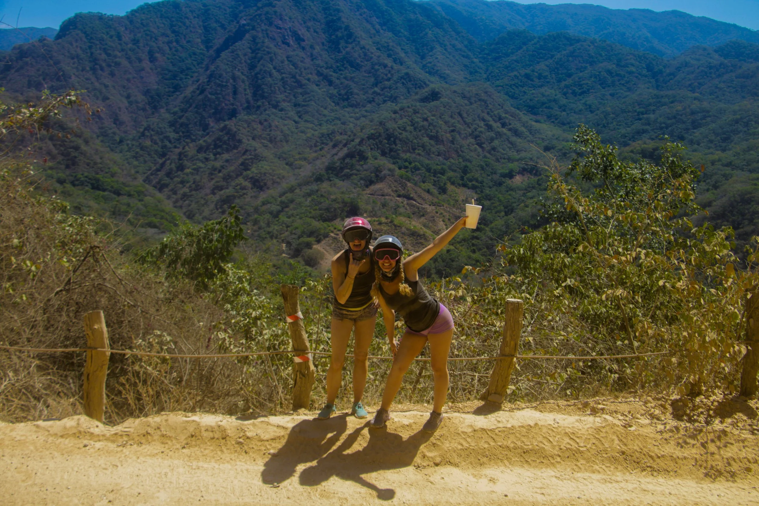 Two girls posing with helmets on, mountains behind, My Deztination adventure.