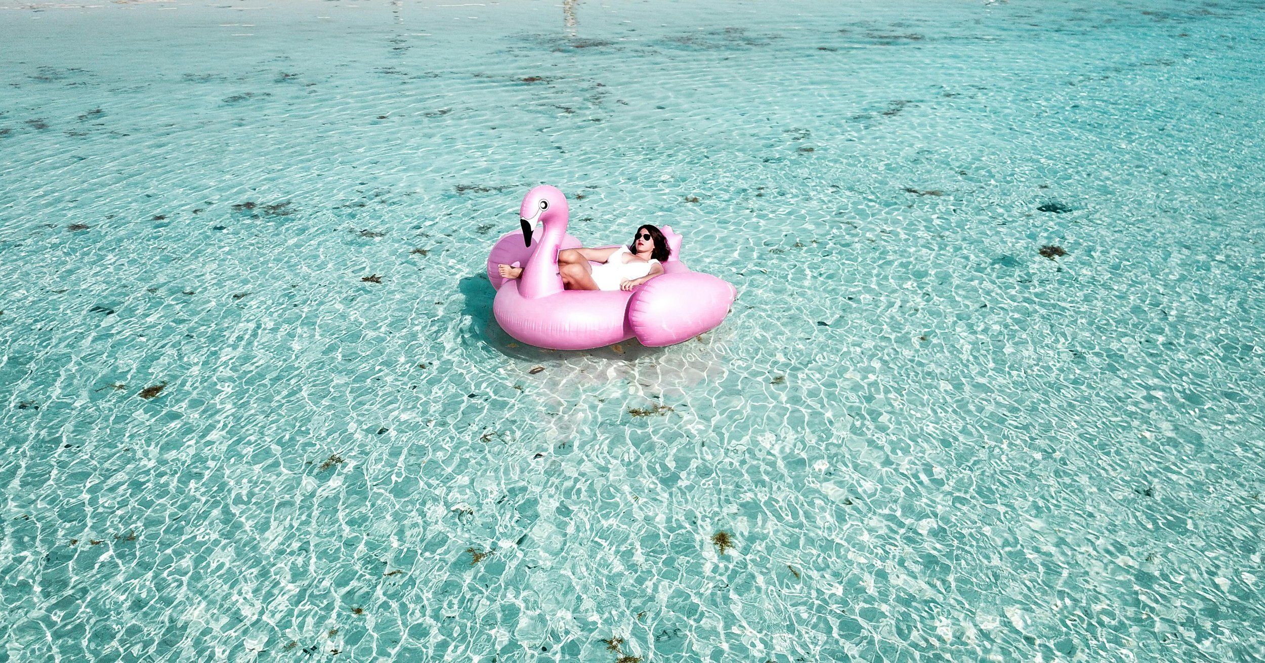 My Deztination client relaxing on an inflatable flamingo on the clear Caribbean waters after relocating to the