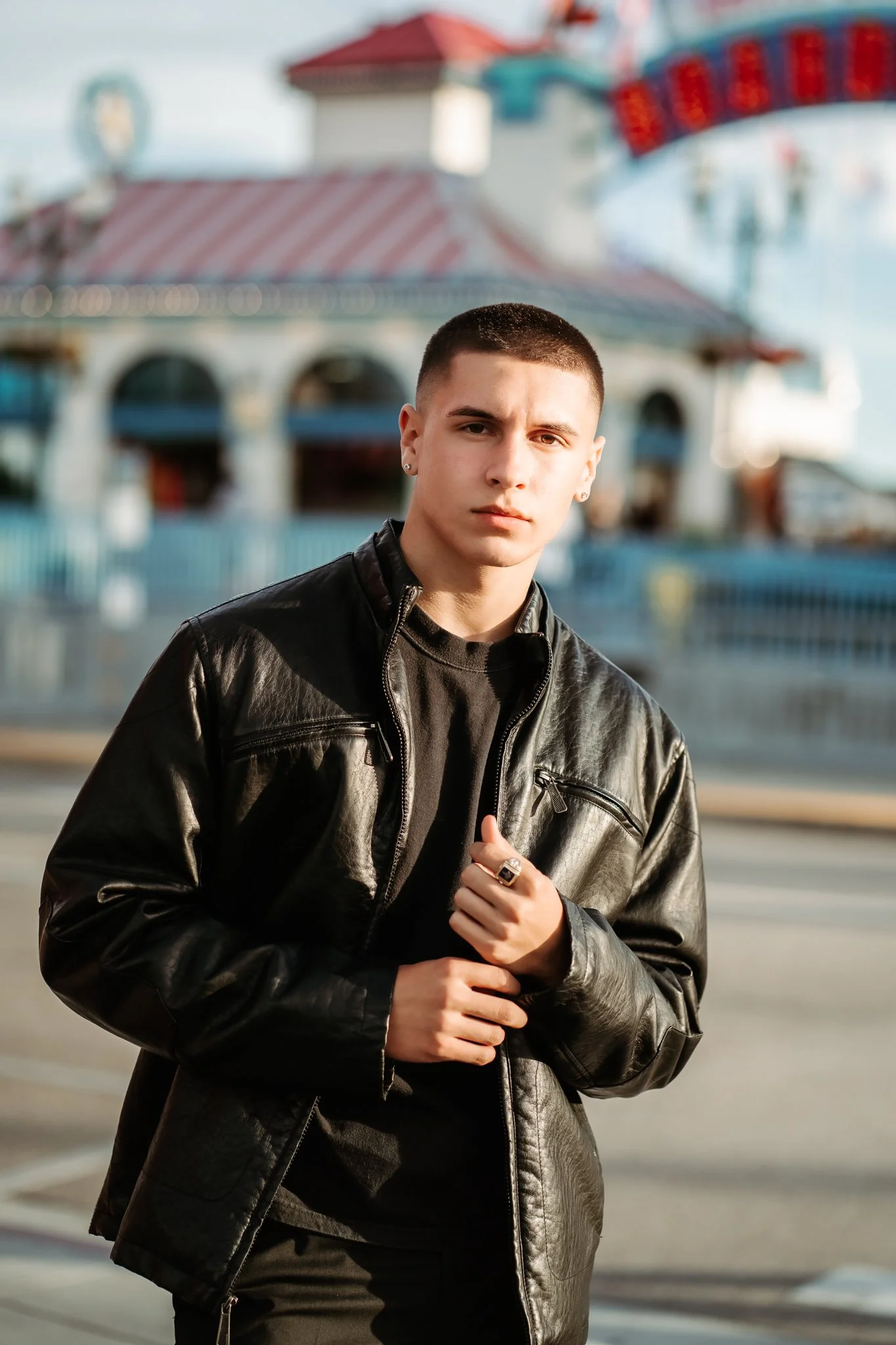 High school senior at the santa cruz boardwalk in California wearing black leather Jacket showing off his Grandpa ring with Military haircut