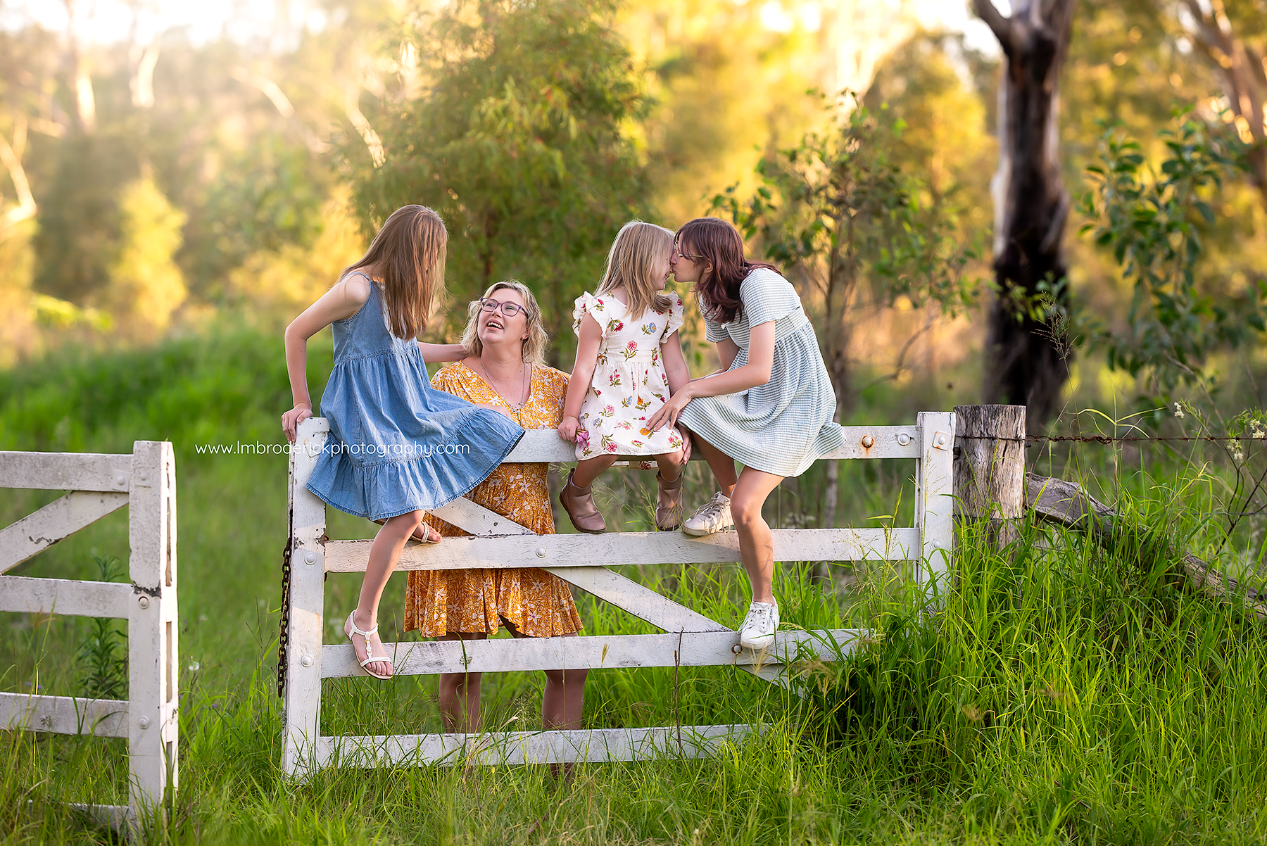 Family of girls sitting on a farm fence laughing