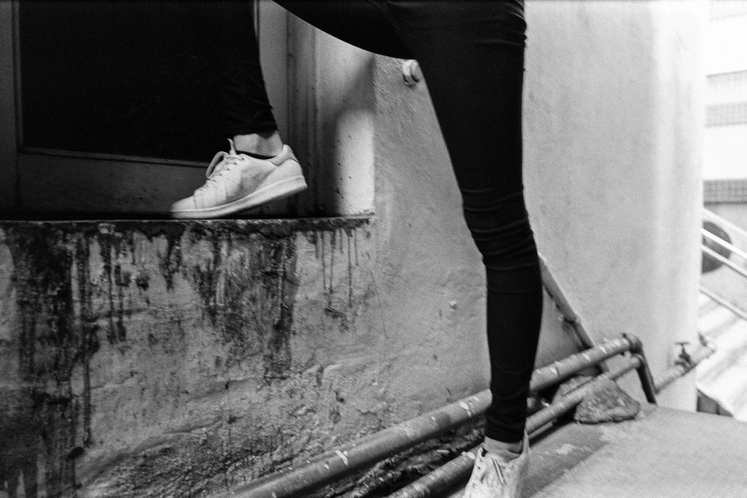 Kodak Tri-X 400 @ 28mm Focal Length - Interacting with the environment by stepping on an edge of a doorway. Compositional variables include wall texture, external plumbing, and stains.
