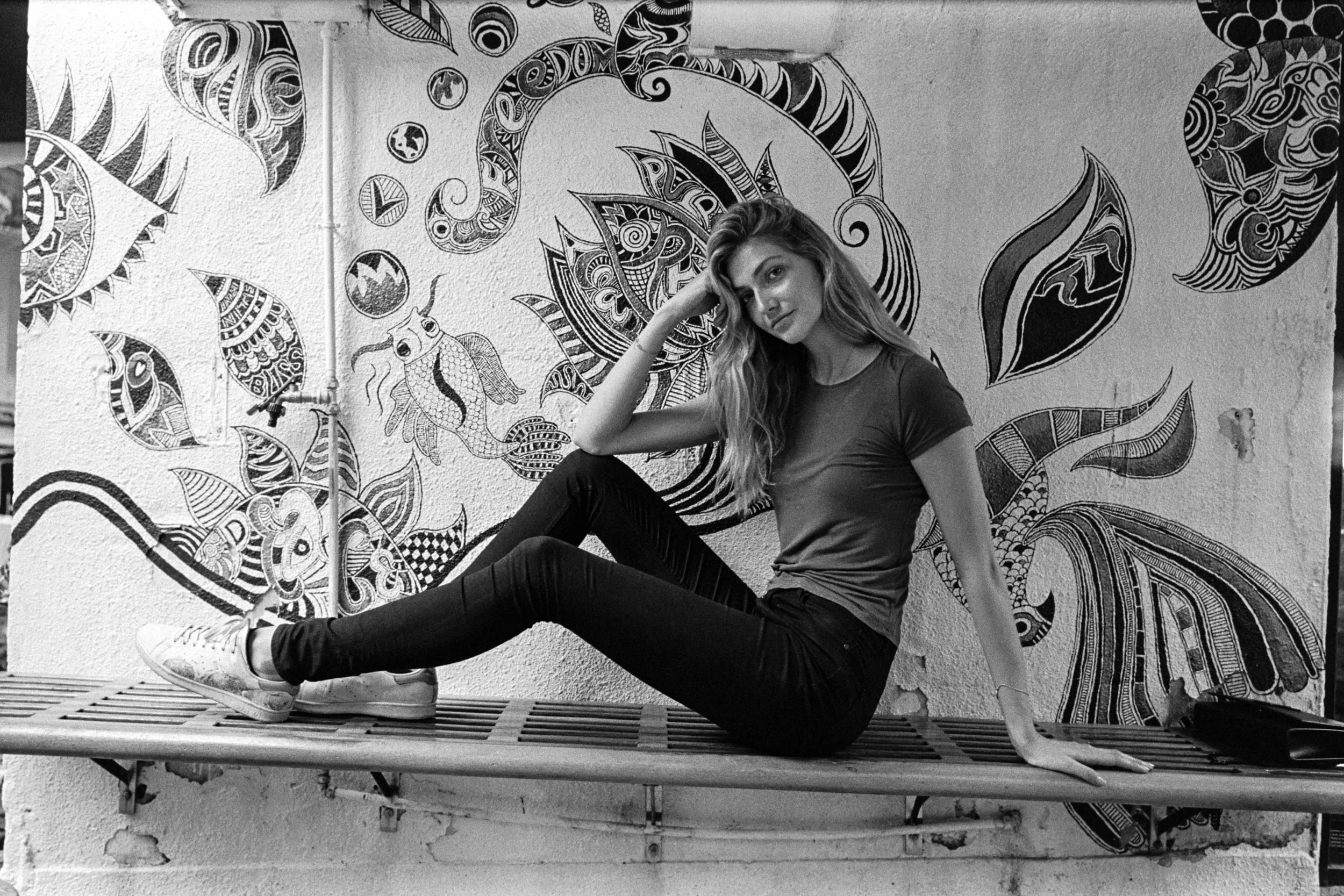 Kodak Tri-X 400 @ 28mm Focal Length - Interacting with the environment by reclining on a metal bench. Compositional variables include background mural.