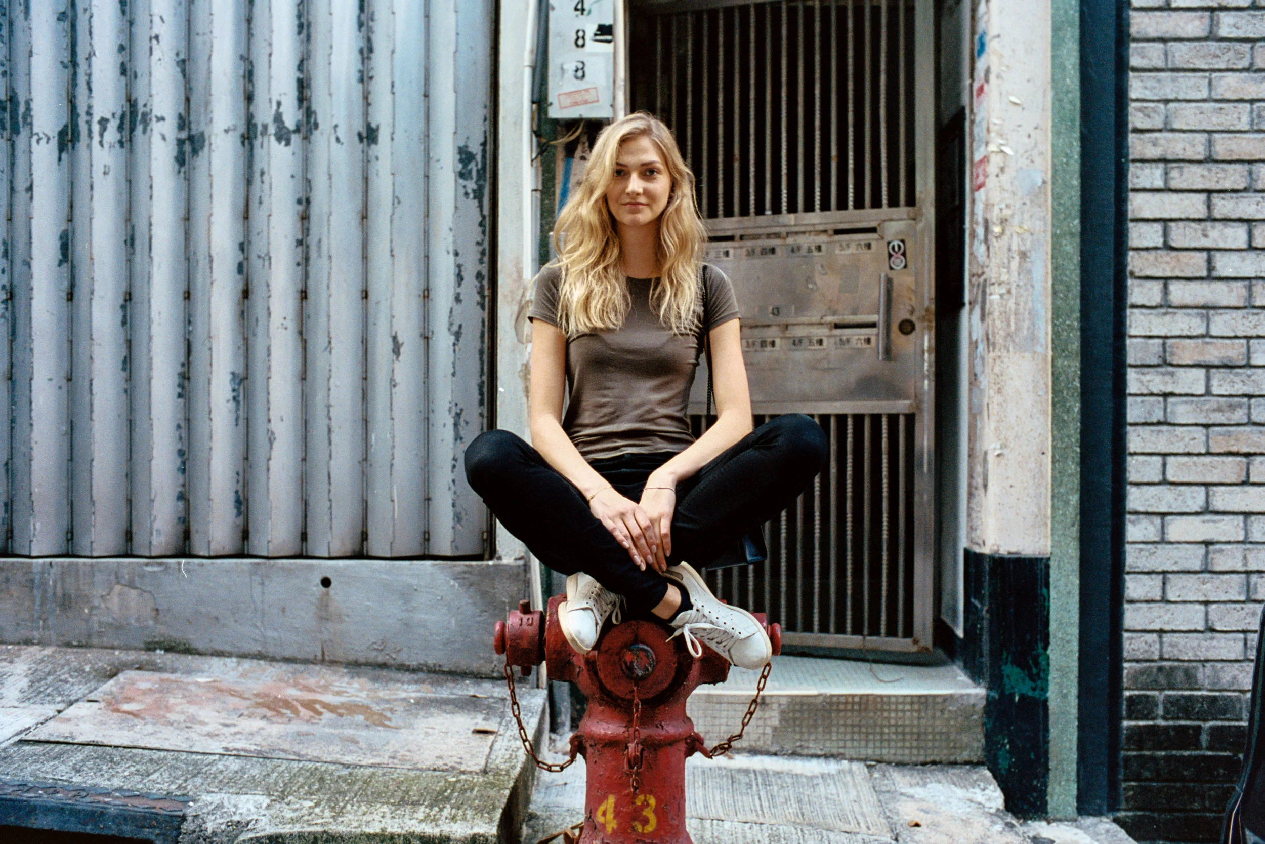 Kodak Portra 400 @ 35mm Focal Length - Interacting with the environment by sitting on a fire hydrant. Compositional variables include brickwork, accordion shutter on storefront, and bars on metal door.