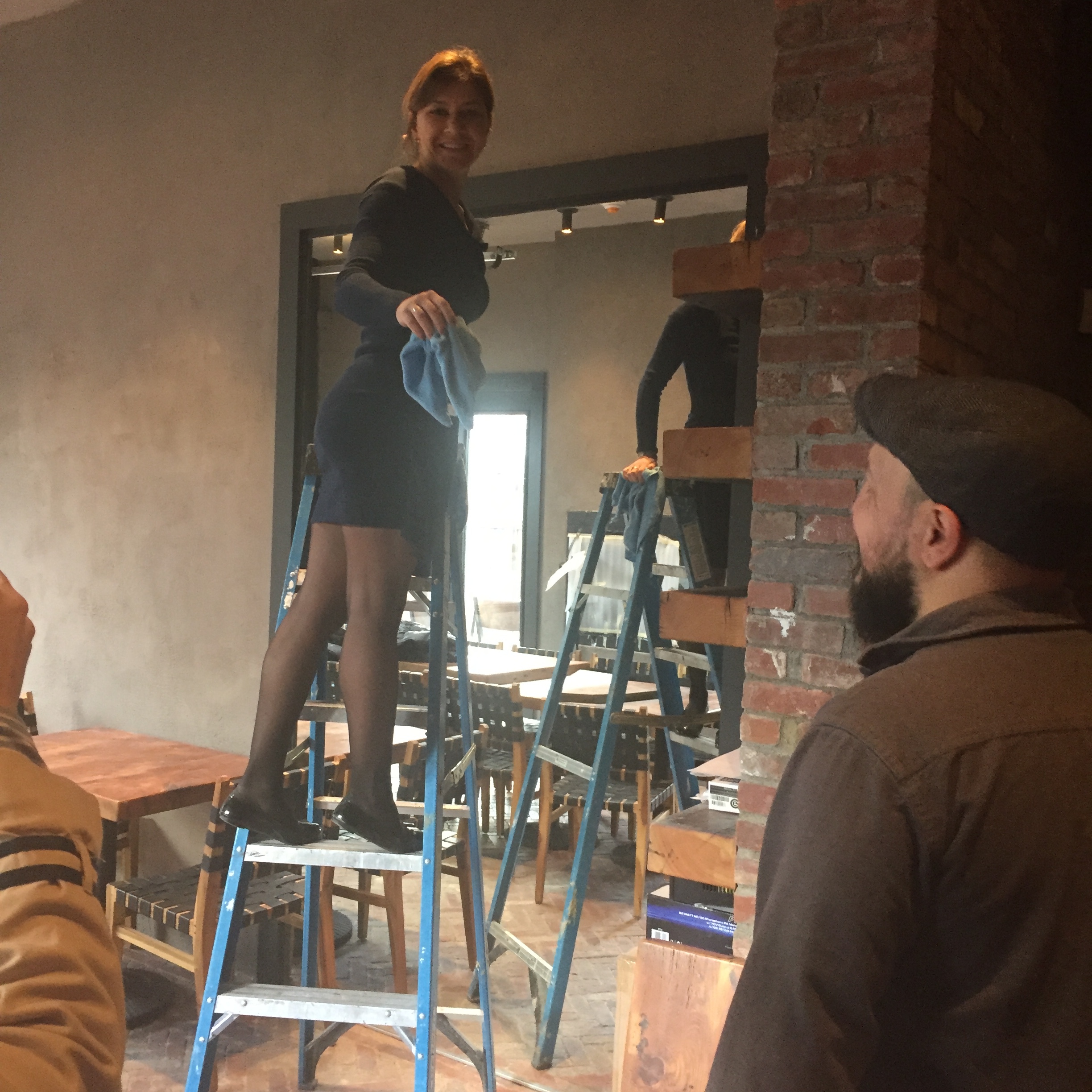 This scene could be one from a musical about the makings of a restaurant, but it is co-owner Alla wiping shelves in preparation for a walk-through by people who were getting sneak peeks of the restaurant before it opened. Photo Credit: Katie Hellmut…